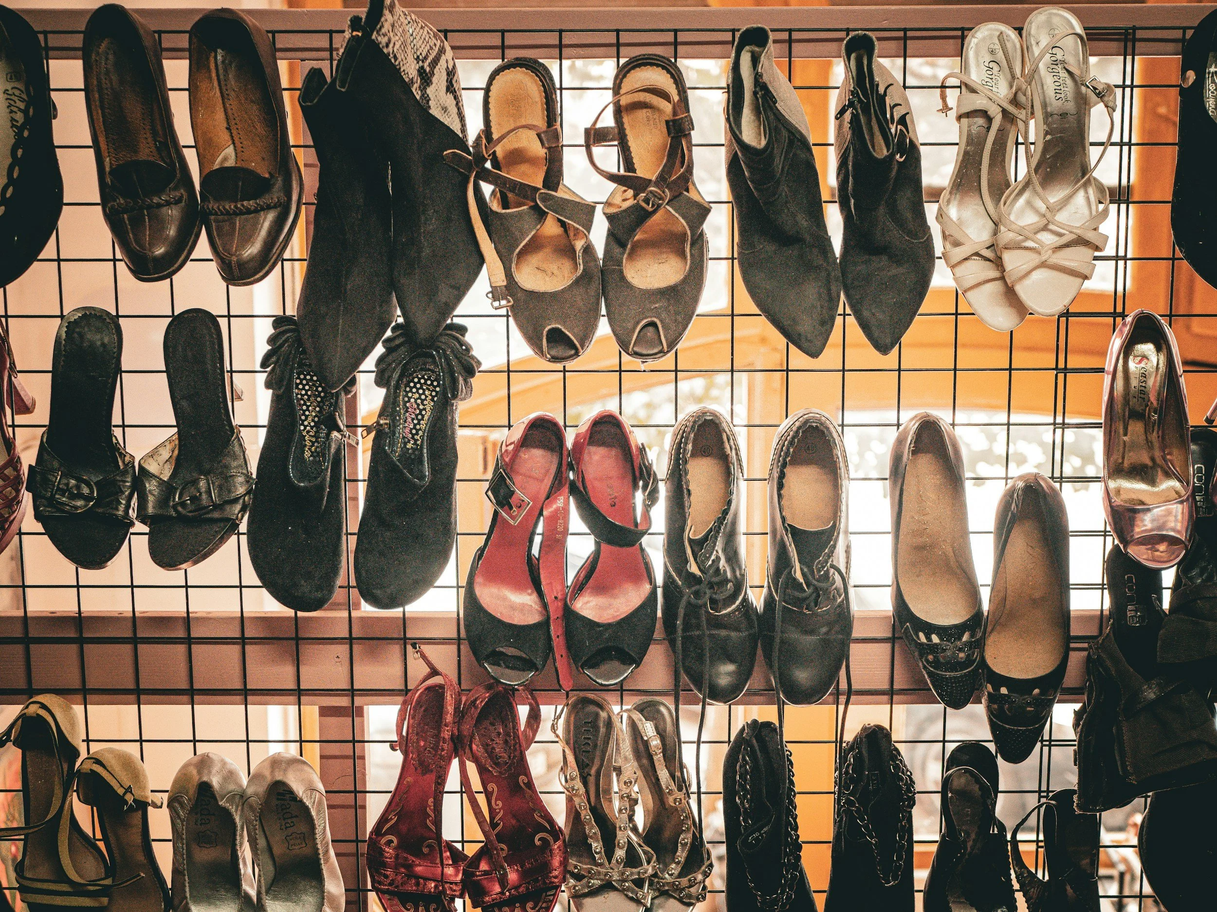 A display of various women's shoes hanging on a black metal grid, including heels, flats, and sandals.
