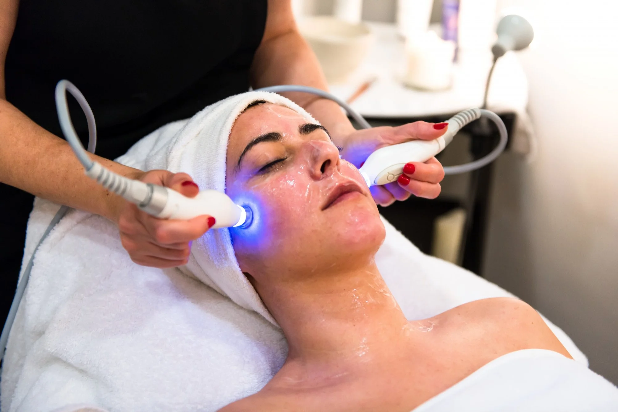 A woman receiving a facial treatment with blue light therapy in a spa or skincare clinic.