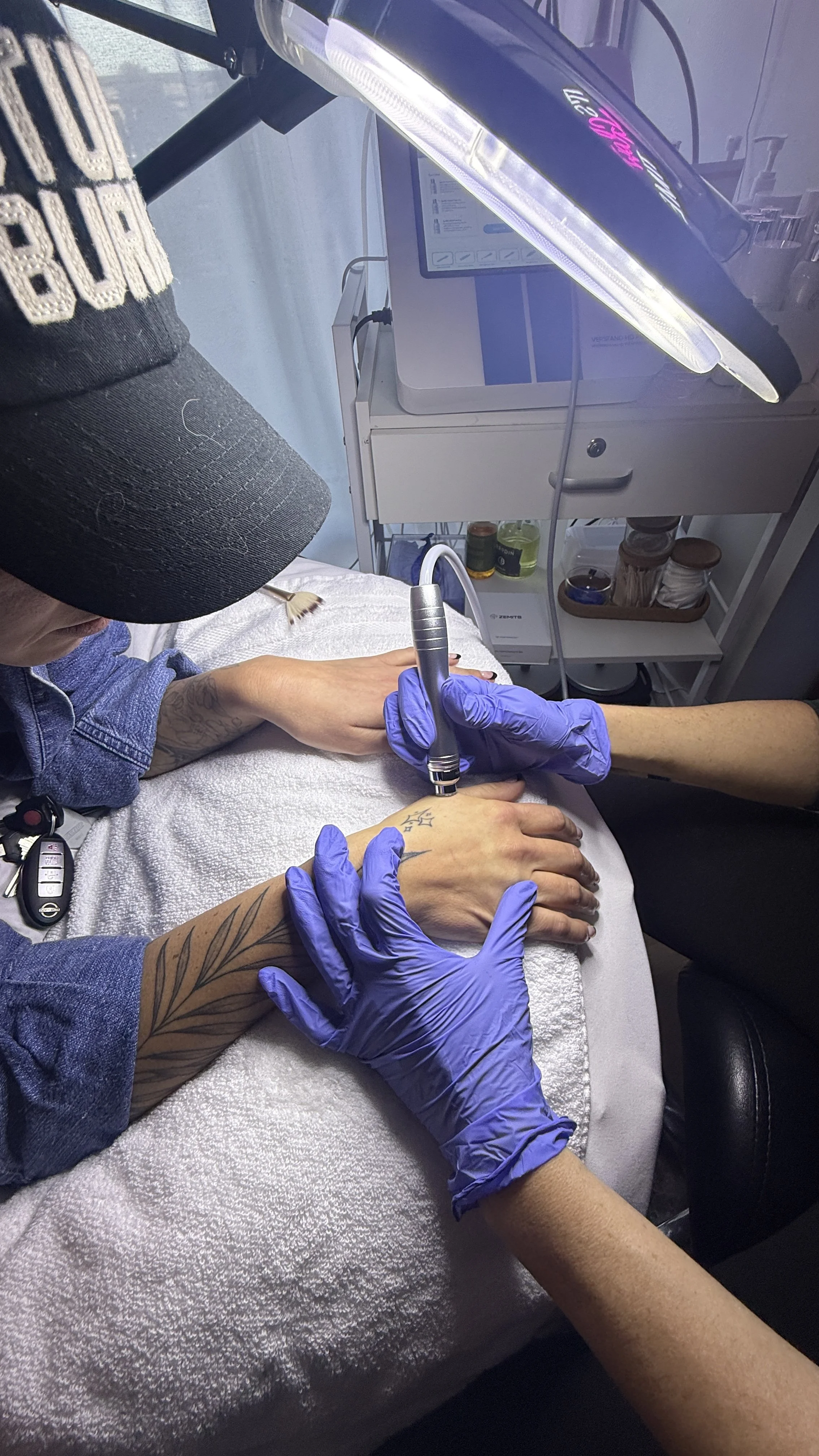 A tattoo artist wearing black gloves is tattooing a floral design on a person's thigh with a tattoo machine.