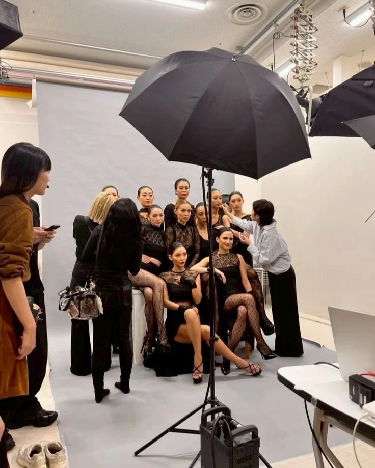 A group of women in black dresses posing for photos in a photo studio with a large black umbrella light and a gray backdrop.