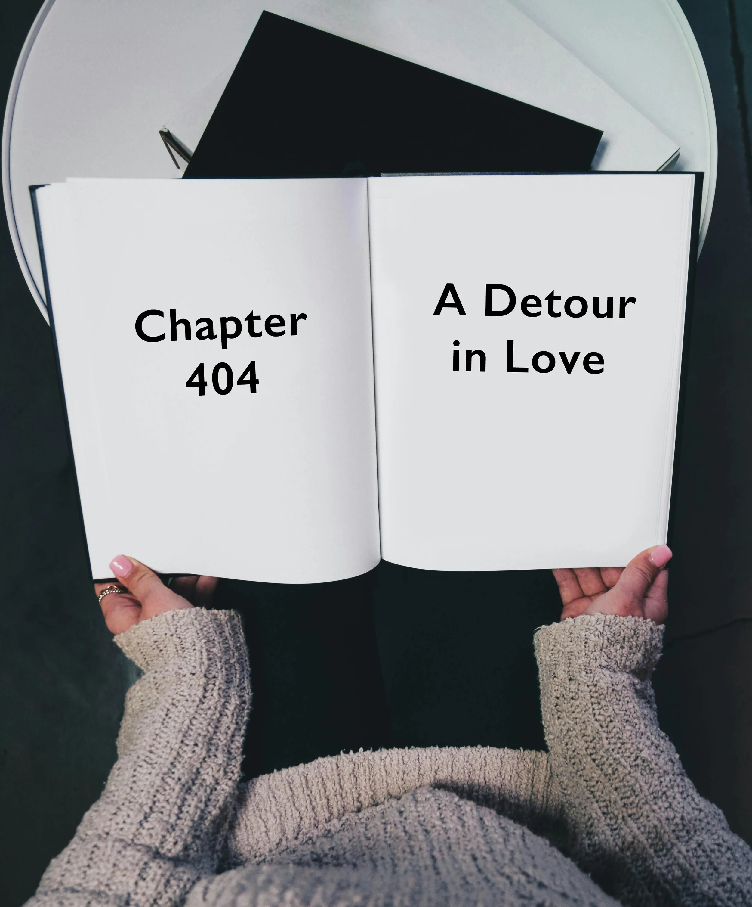 Open book displaying chapter 404 titled 'A Detour in Love', held by person wearing beige sweater, placed on a white round table with black and white books in background.