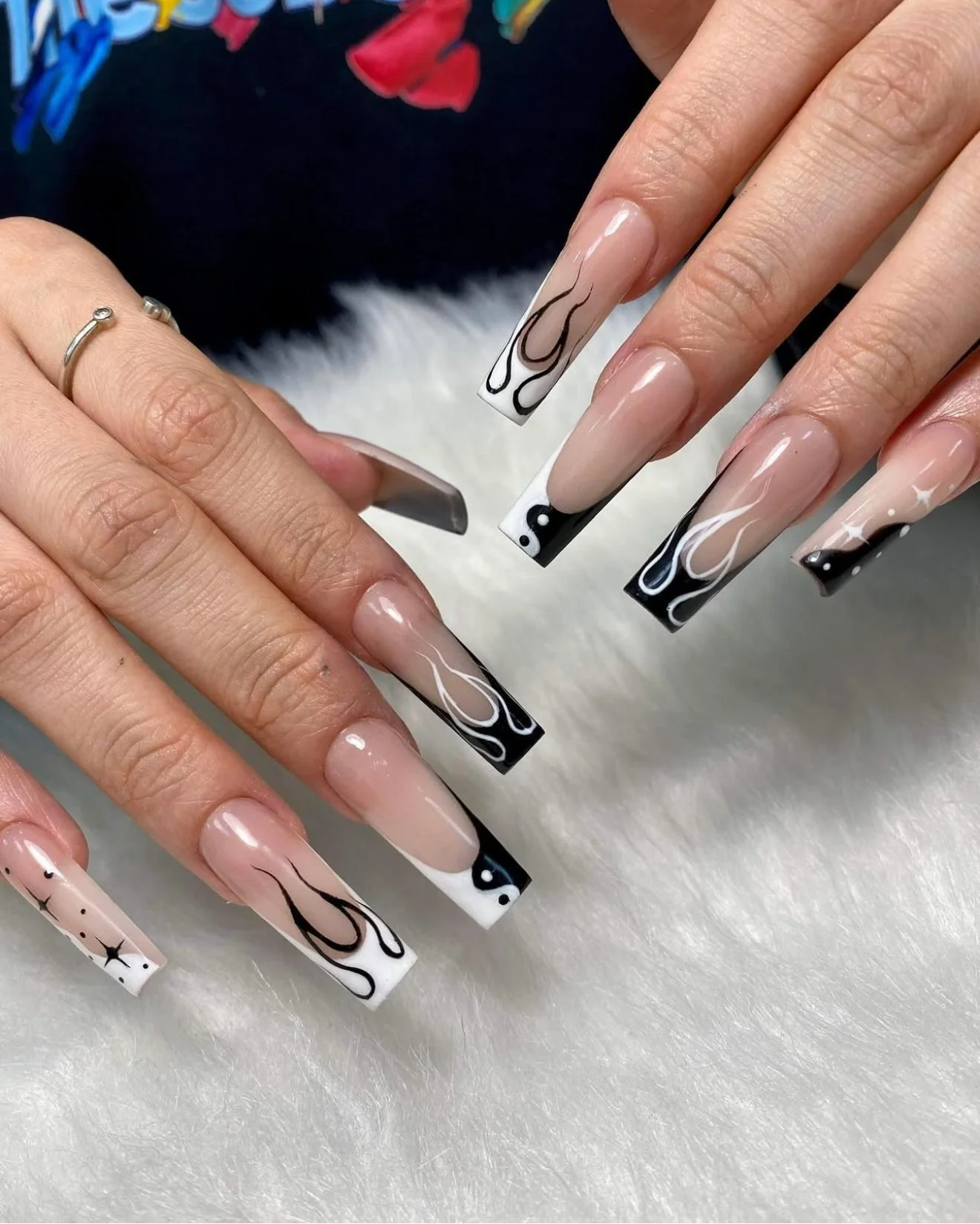 Close-up of hands with long square-shaped acrylic nails featuring marble and black and white swirl designs, on a white furry surface.