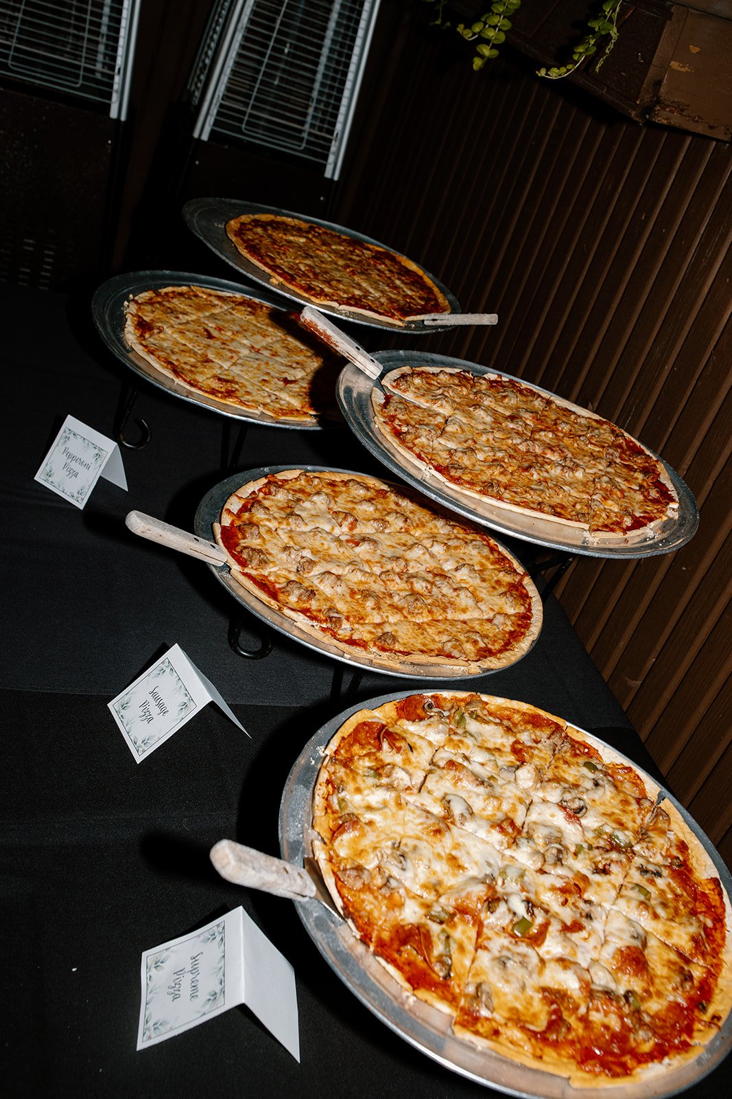 Five different pizzas on display at a buffet table, labeled Pepperoni, Cheese, and Veggie.