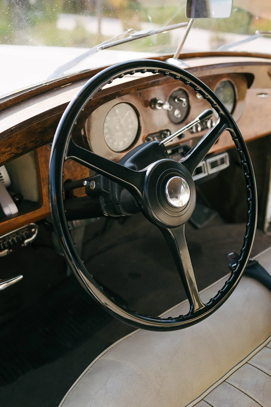 Inside a vintage car, focusing on the steering wheel and dashboard with wooden paneling and analog gauges.