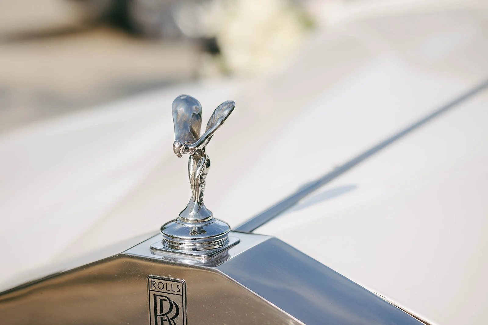 A close-up of a silver hood ornament of a Rolls Royce car, depicting a woman with wings, standing on a round base.