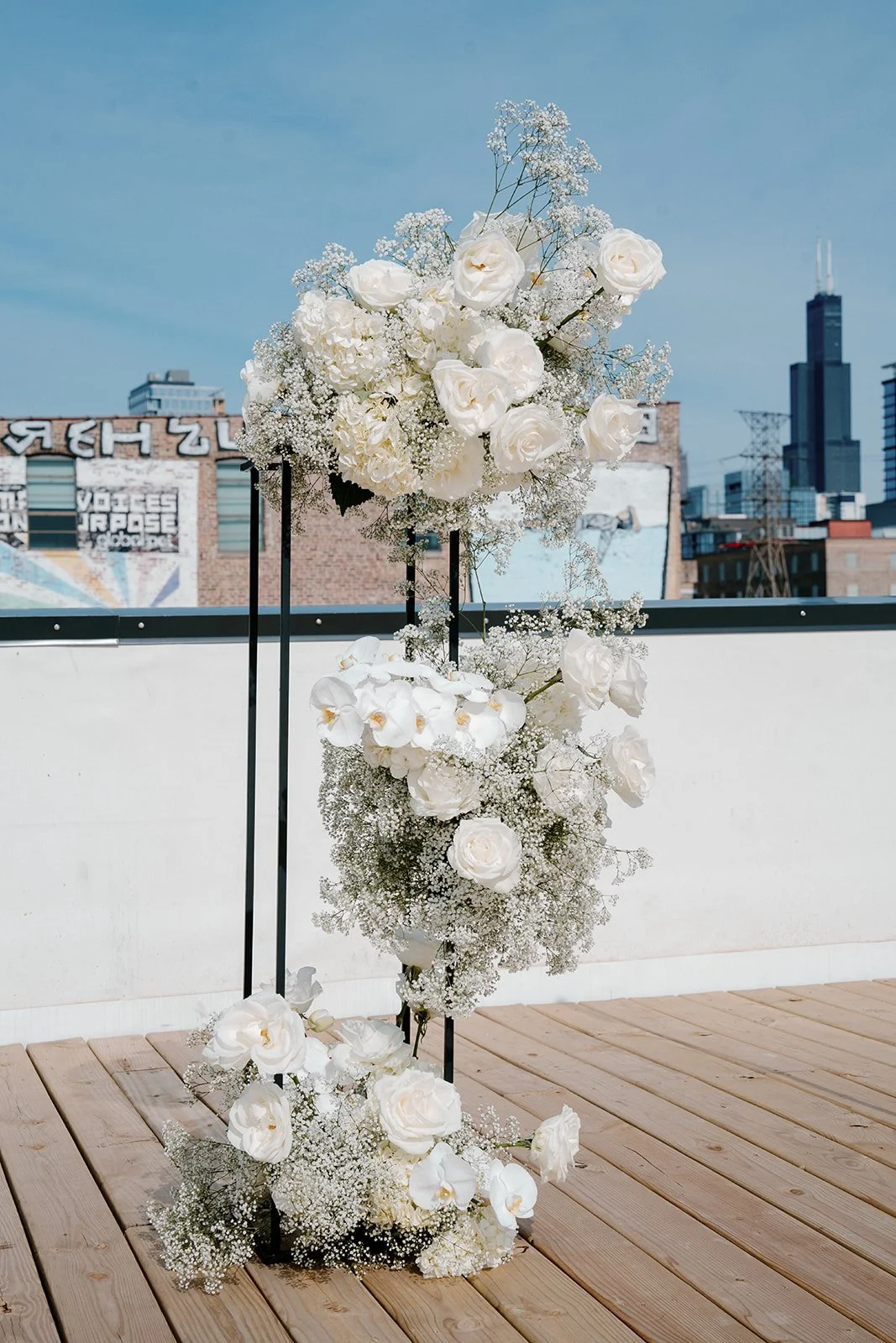 White floral arrangement with roses and baby's breath on a rooftop against city skyline.