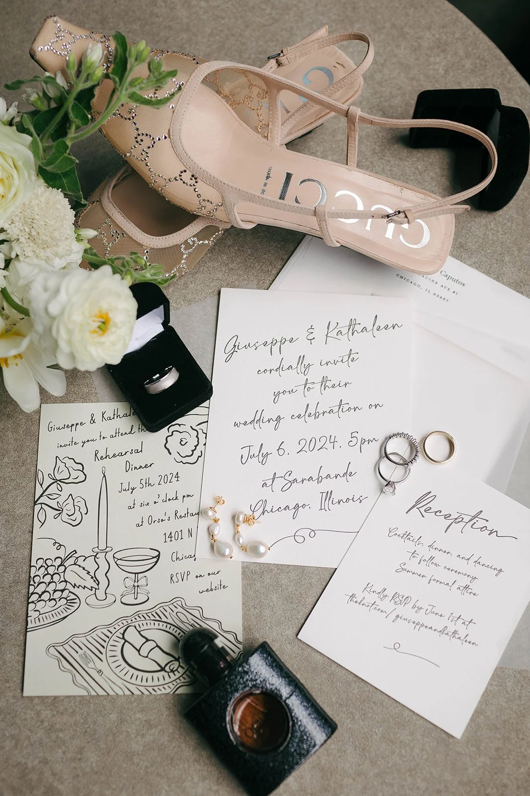Wedding invitation, rings, bouquet, perfume, and accessories on a table.