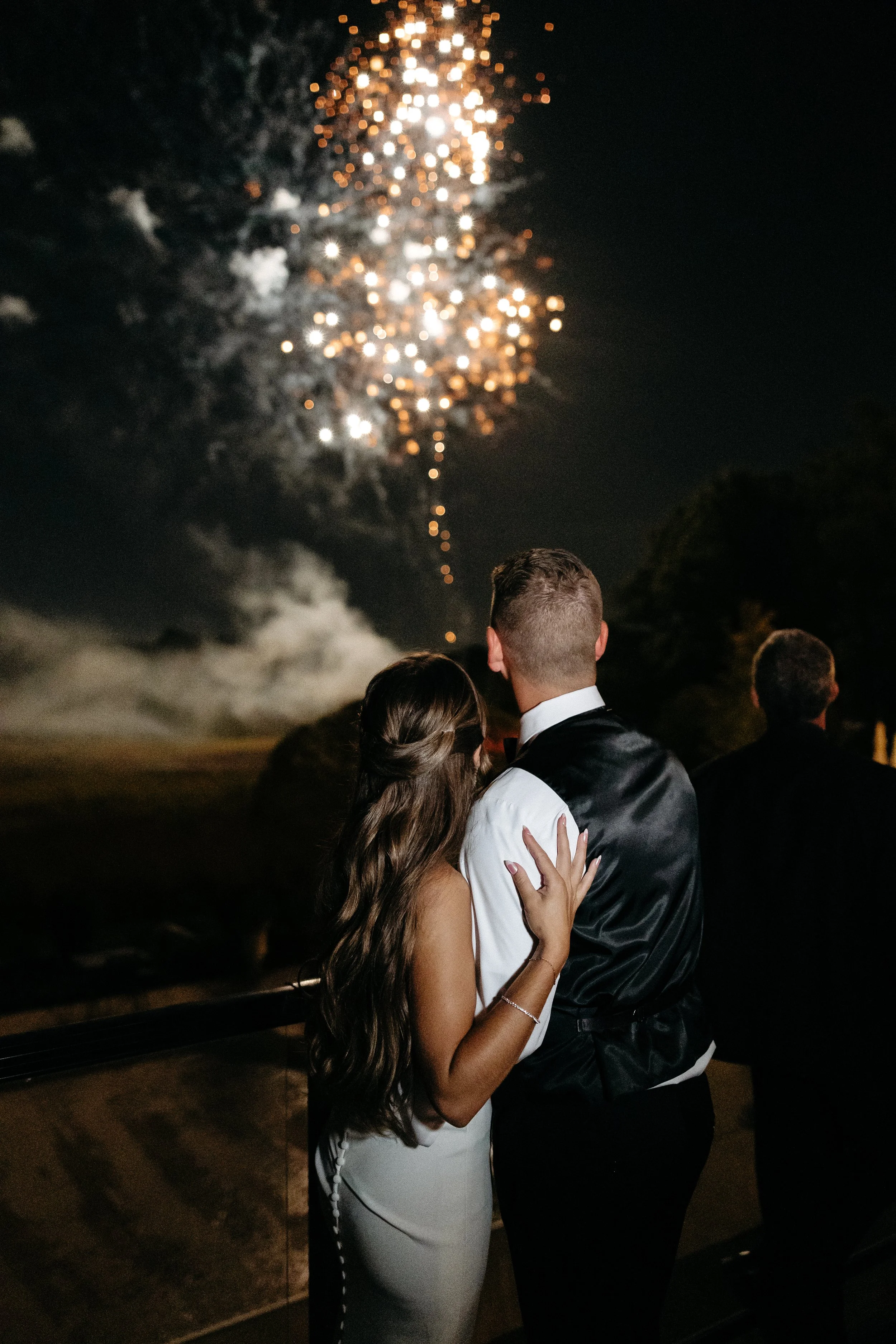 Couple watching fireworks at night, with fireworks bursting in the sky above.