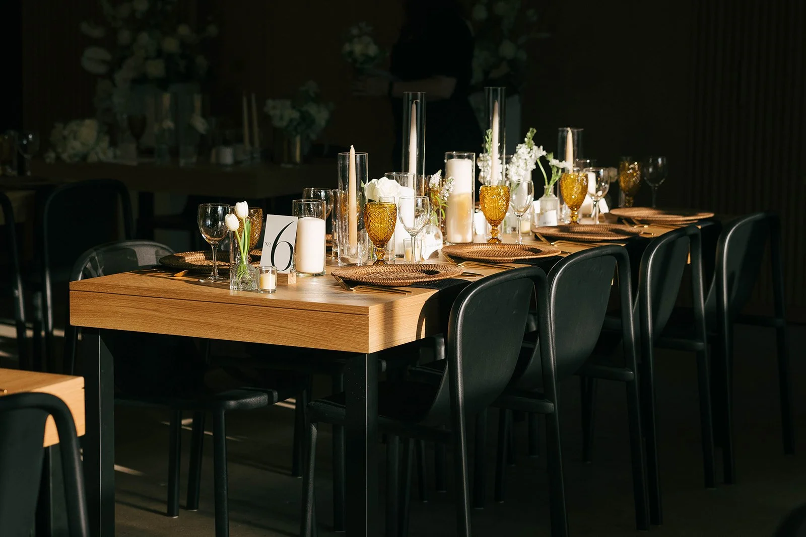 Elegant banquet table set with candles, glassware, white flowers, and table number 6, in a dimly lit room for a formal event.
