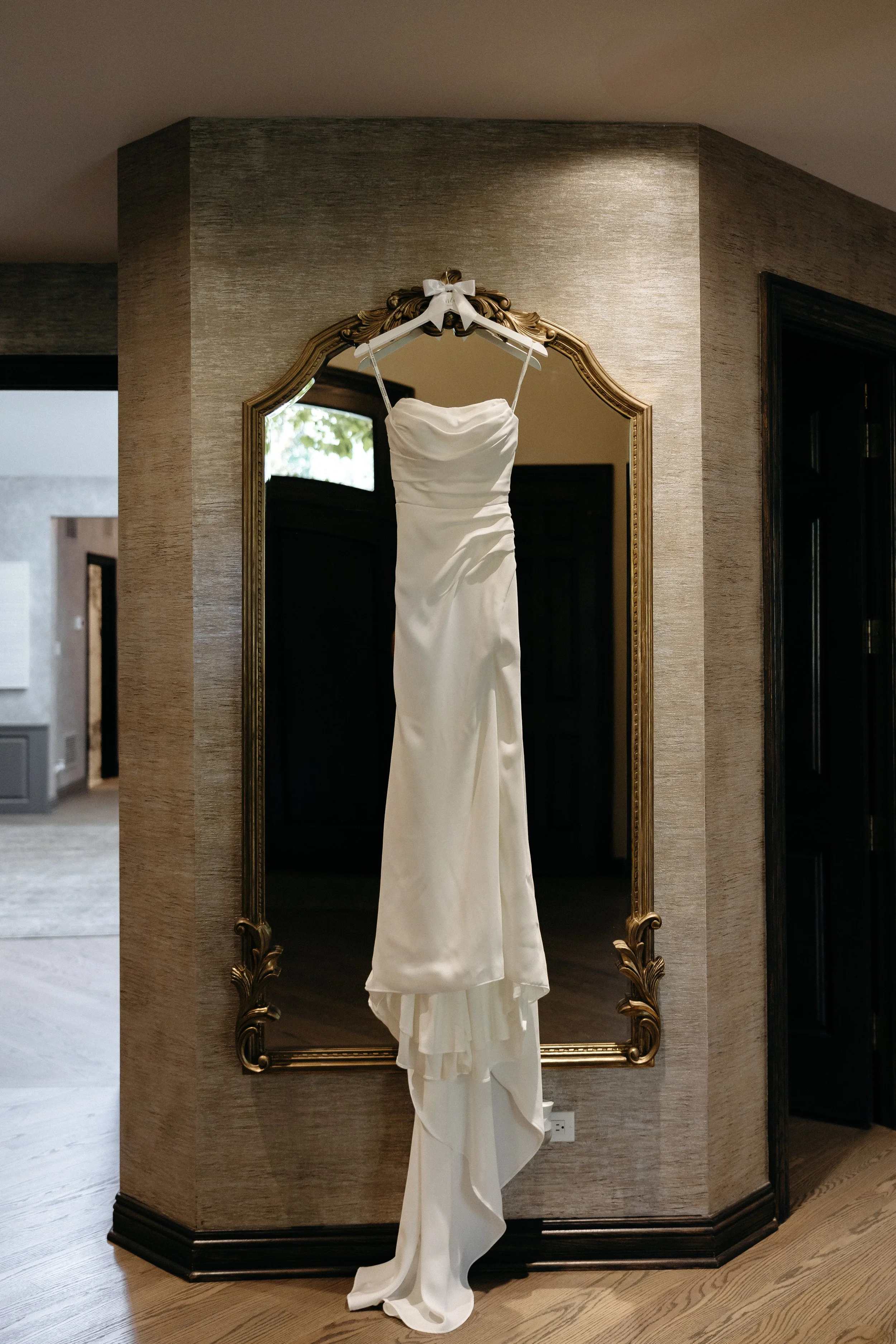 A white wedding dress hanging on a decorative gold mirror in a room.