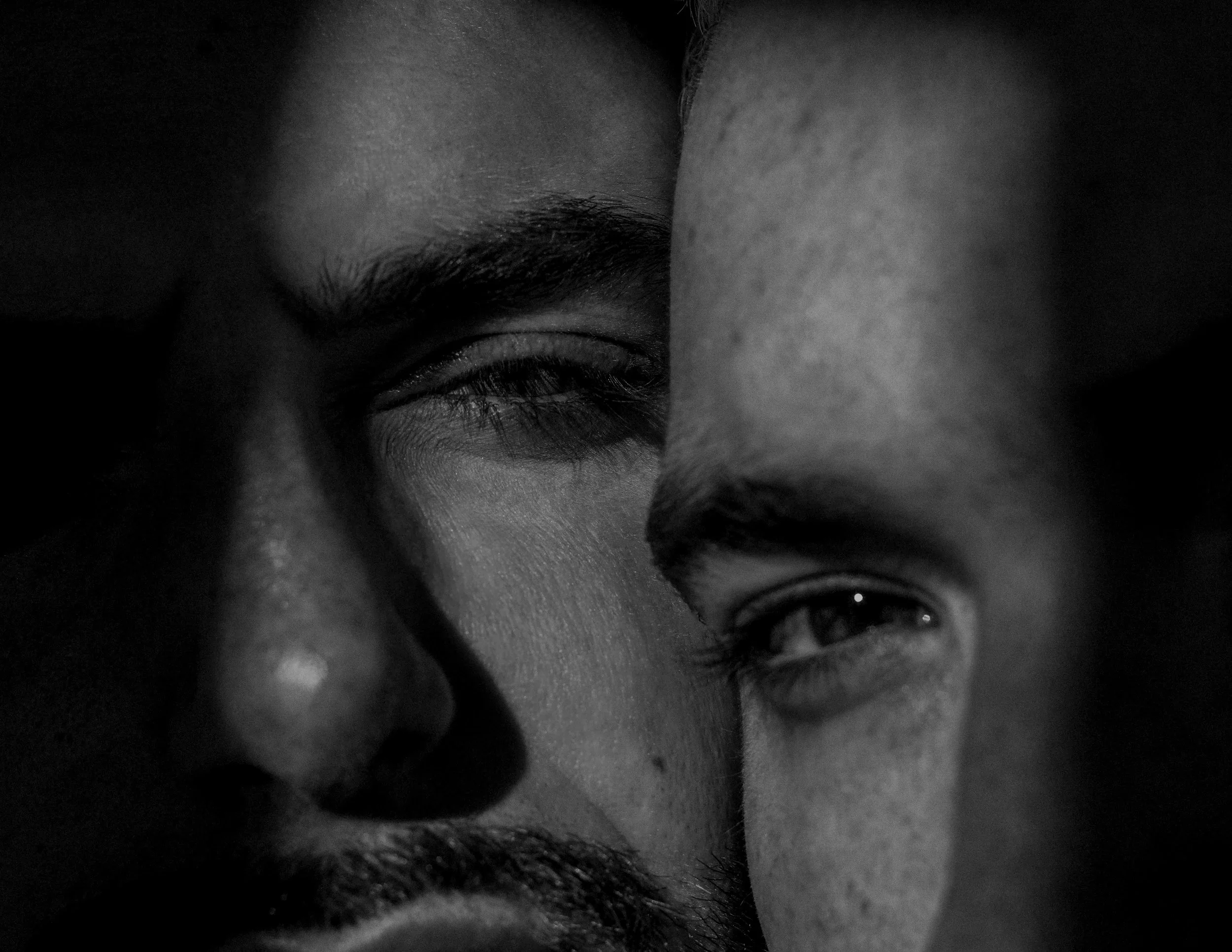 Gros plan de deux visages, une personne avec un visage sombre et une autre en clair, en noir et blanc, très proche.