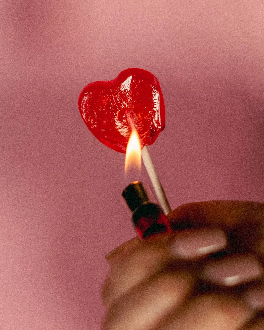 Une main tenant un bâtonnet d'allumettes, dont la tête en forme de cœur en cire rouge est enflammée.