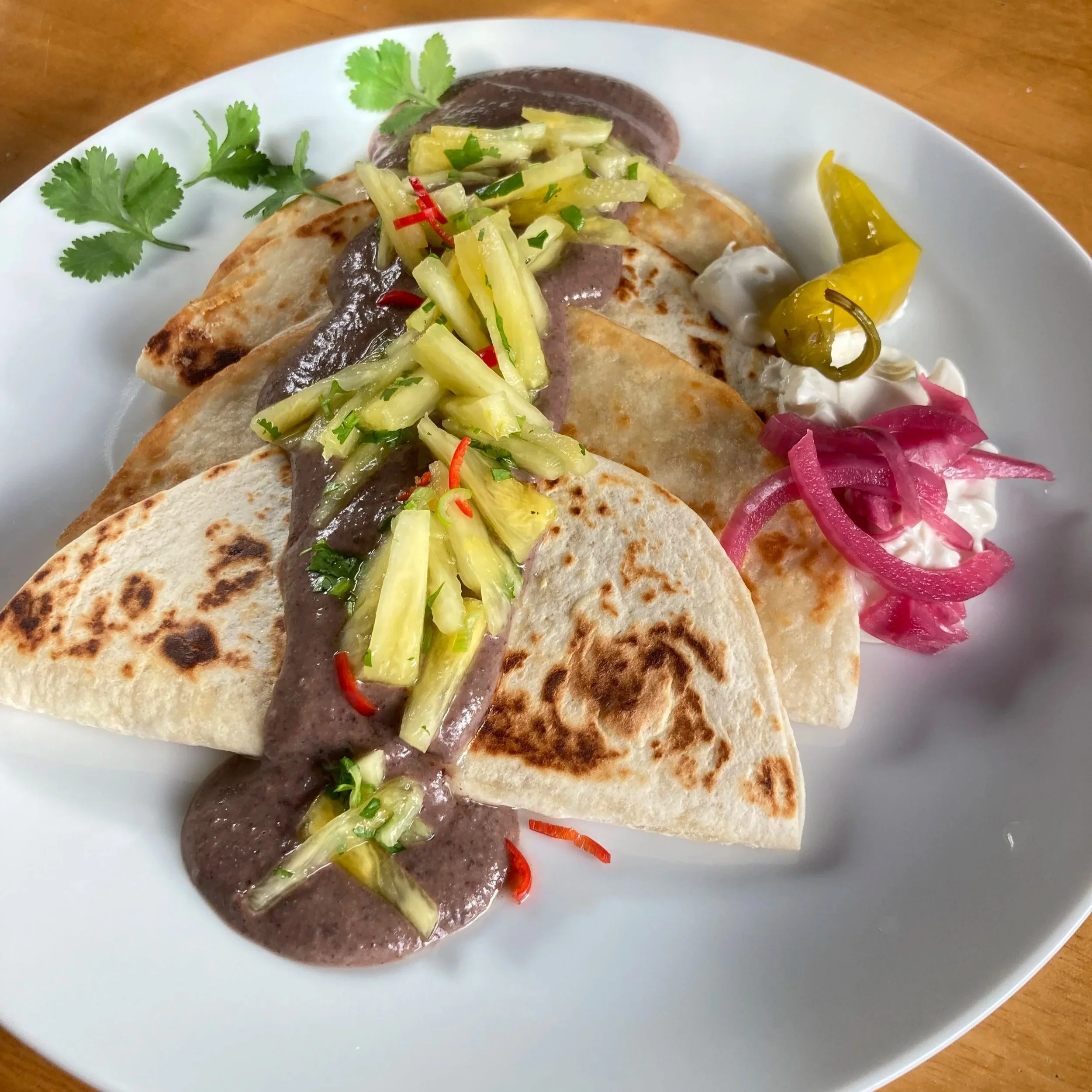 Vegan enfrijoladas with pineapple salsa, black bean sauce, pink pickled onions and pickled chilli