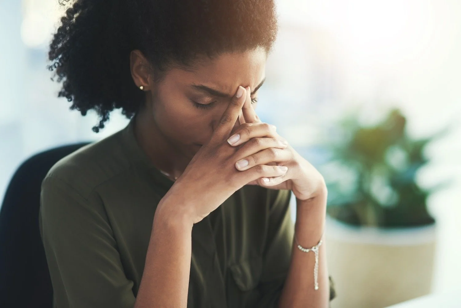 High-achieving woman sitting with her head in her hands, feeling exhausted and overwhelmed by the pressure of always being the strong one.