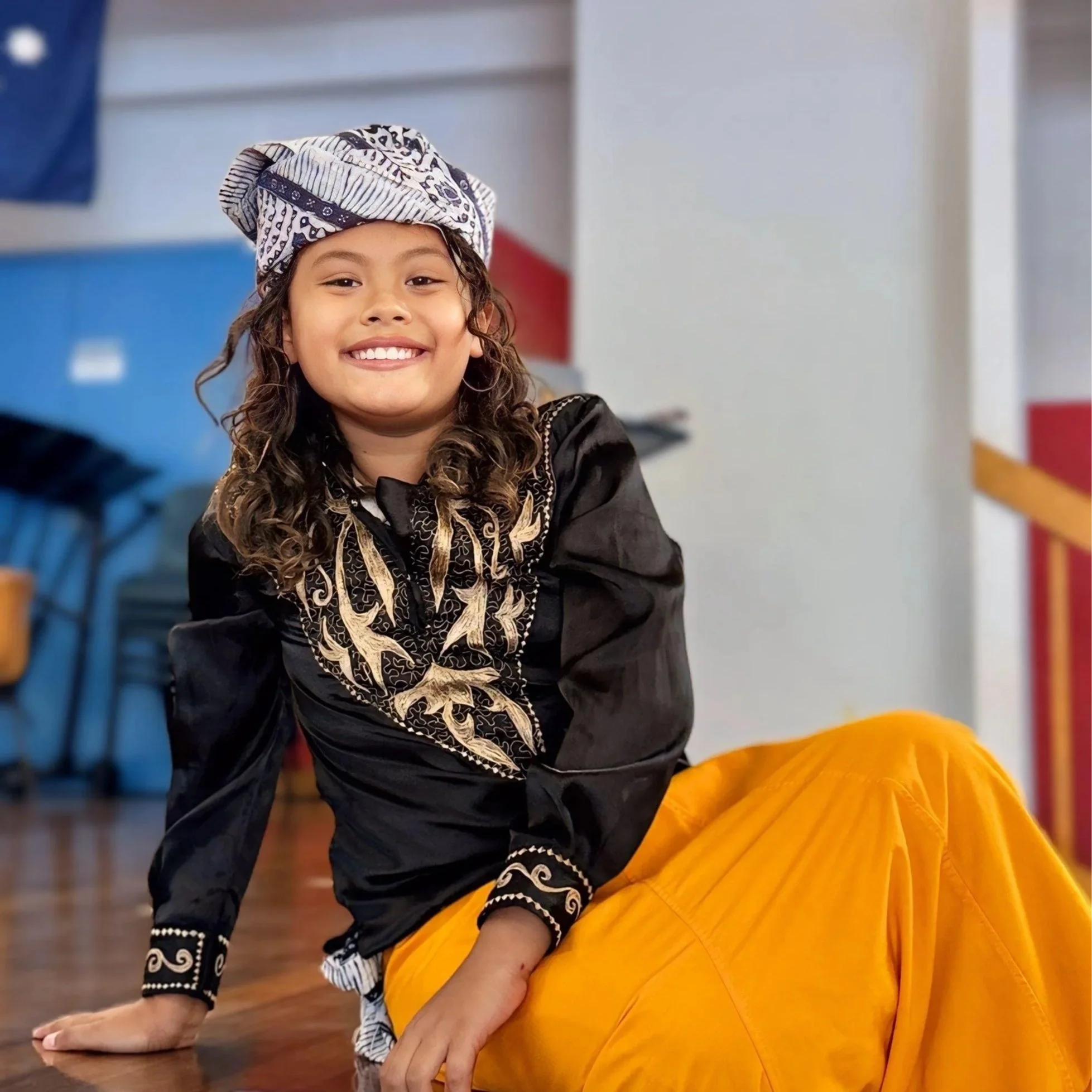 A young boy with curly hair wearing black Acehnese costume and yellow costume pants