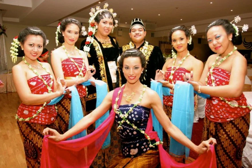 Group of people dressed in traditional Batak attire, adorned with floral accessories, posing indoors for a cultural event or celebration.