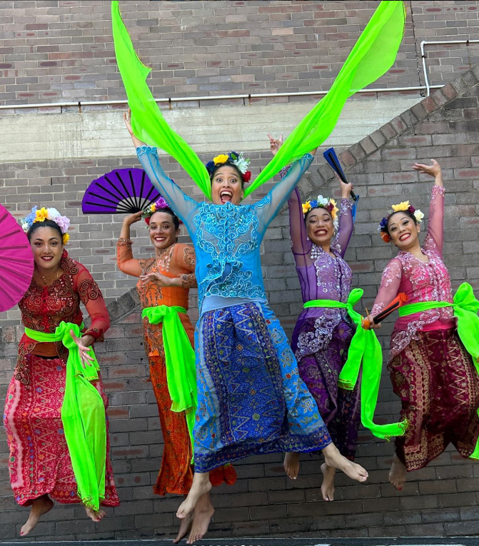 Five women in brightly coloured Indonesian costumes are jumping in the air and laughing