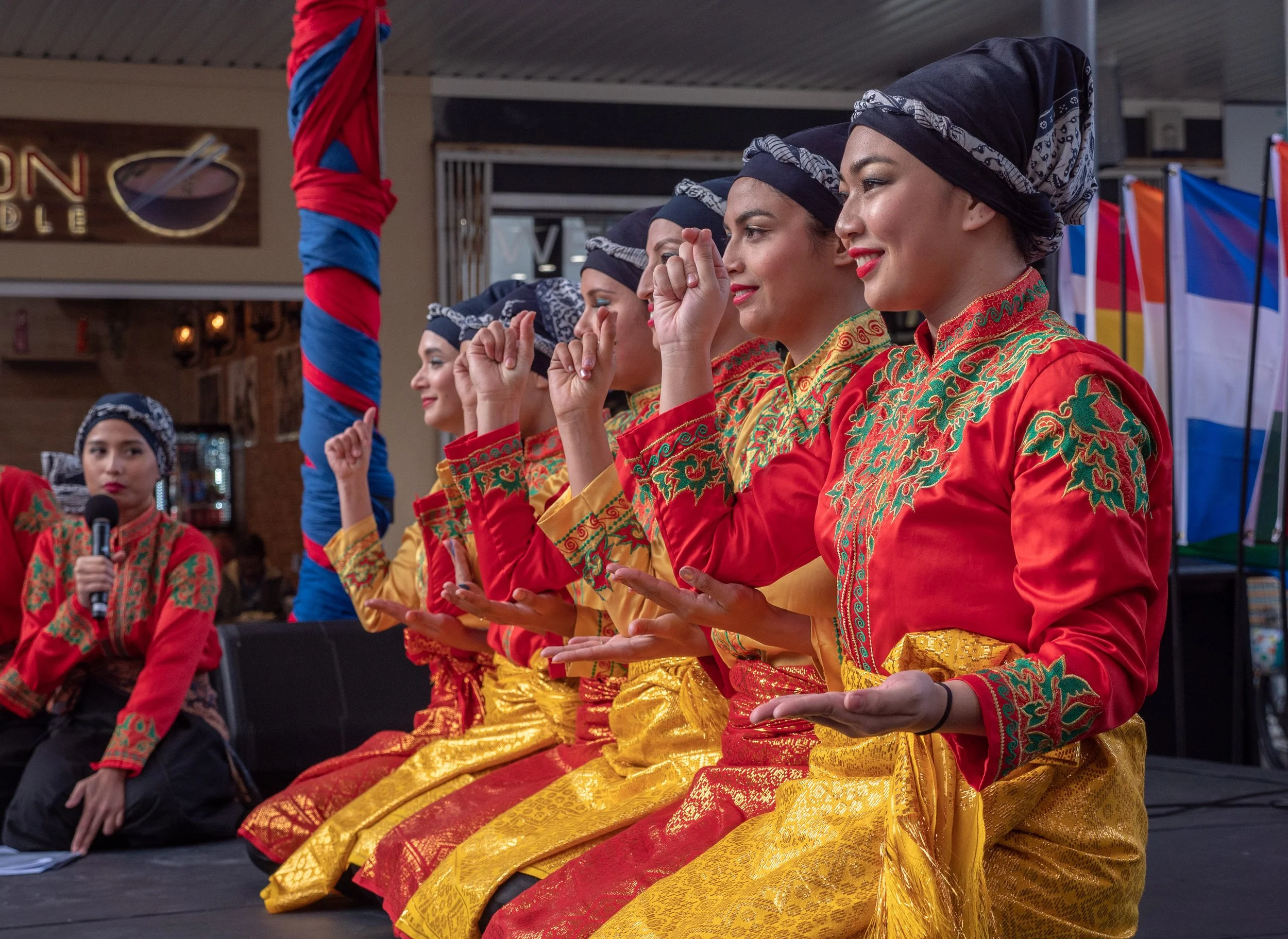 Group of women dressed in traditional Indonesian attire performing a seated dance on stage
