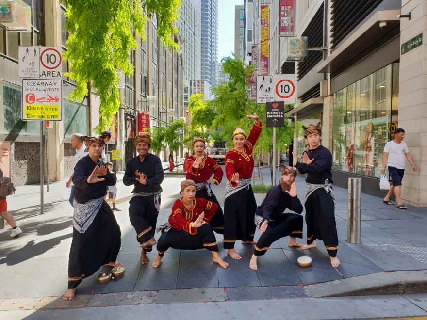Seven street performers in traditional Indonesian clothing posing in a busy city street.