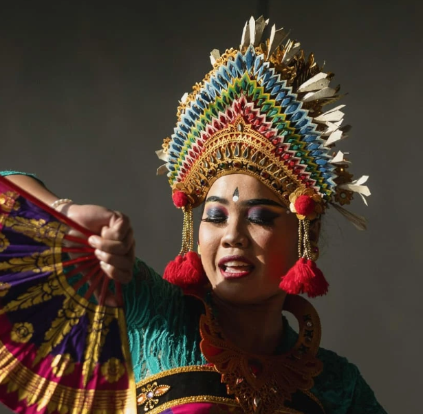 A performer dressed in elaborate traditional costume with a large, colorful feathered headdress, holding a decorated fan