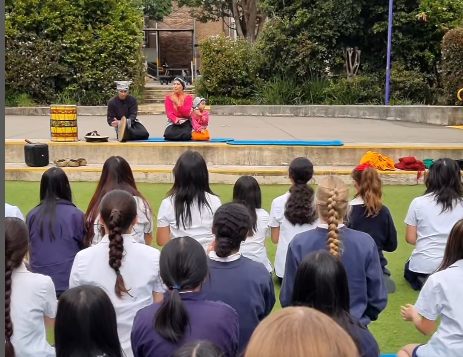 A group of students watching a  performance outdoors.