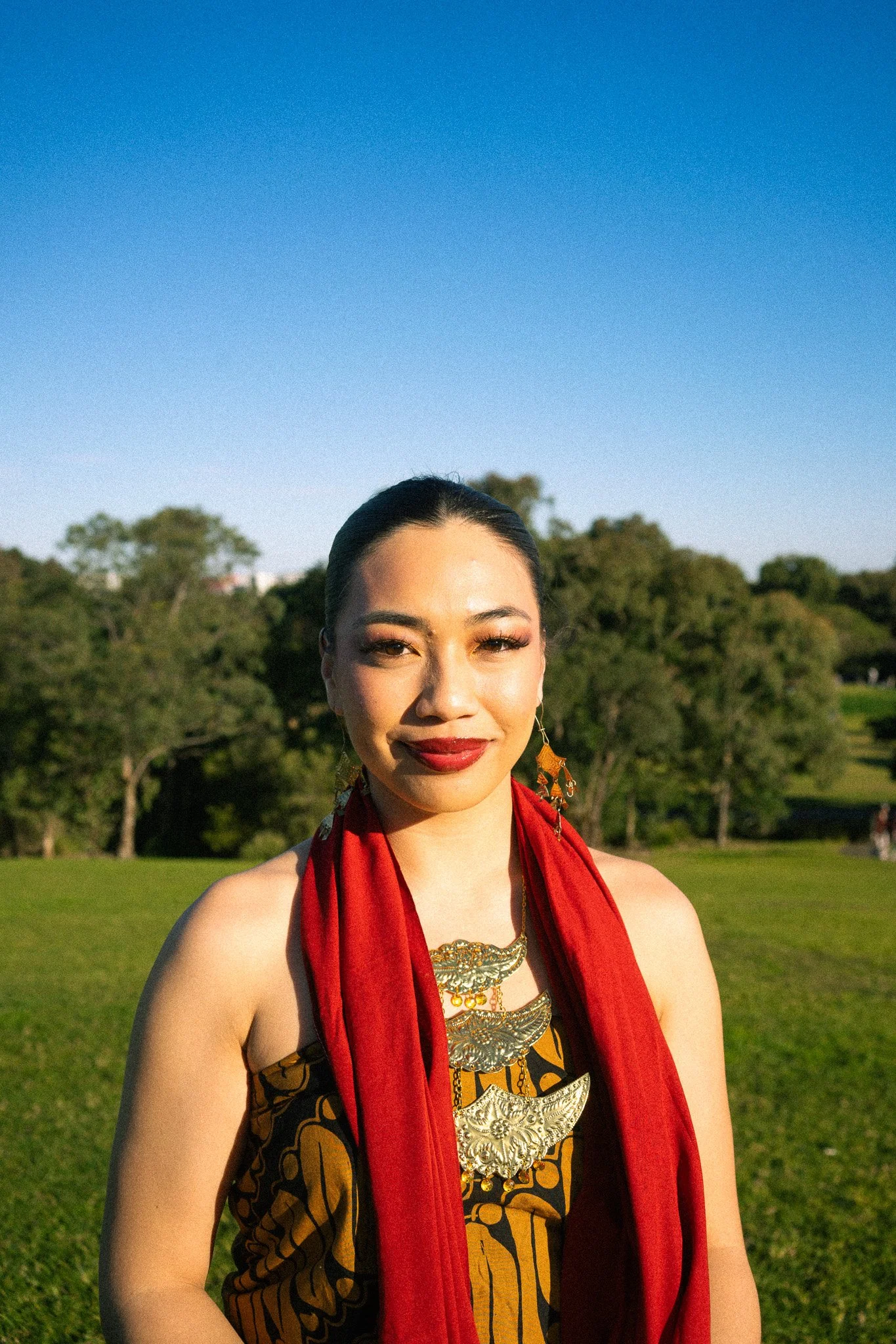 A woman with long dark hair, hoop earrings, and dark lipstick posing against a light background.