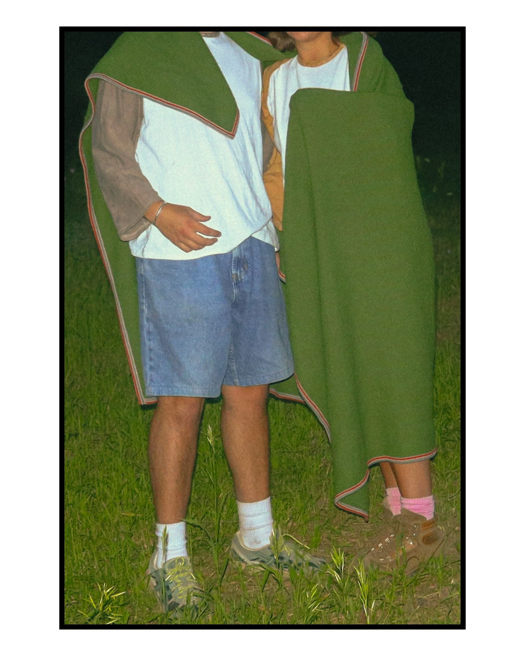 Close-up of two people standing outdoors on grass, wearing casual clothes and green robes.