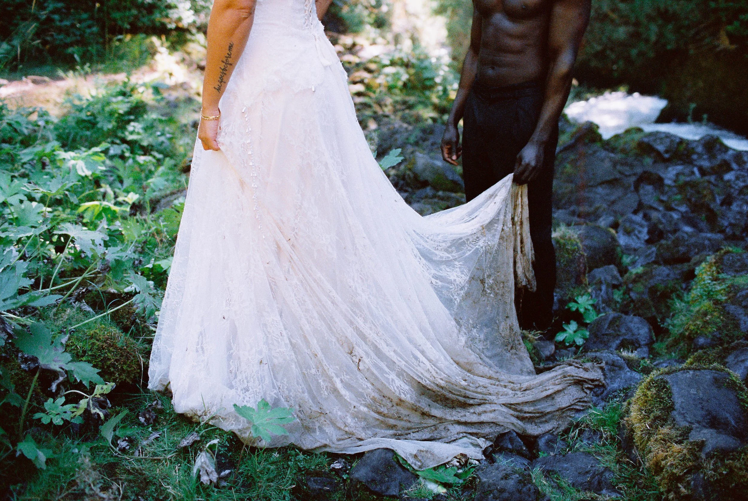 A wedding dress draped over a rock in a forest setting with greenery and a creek.