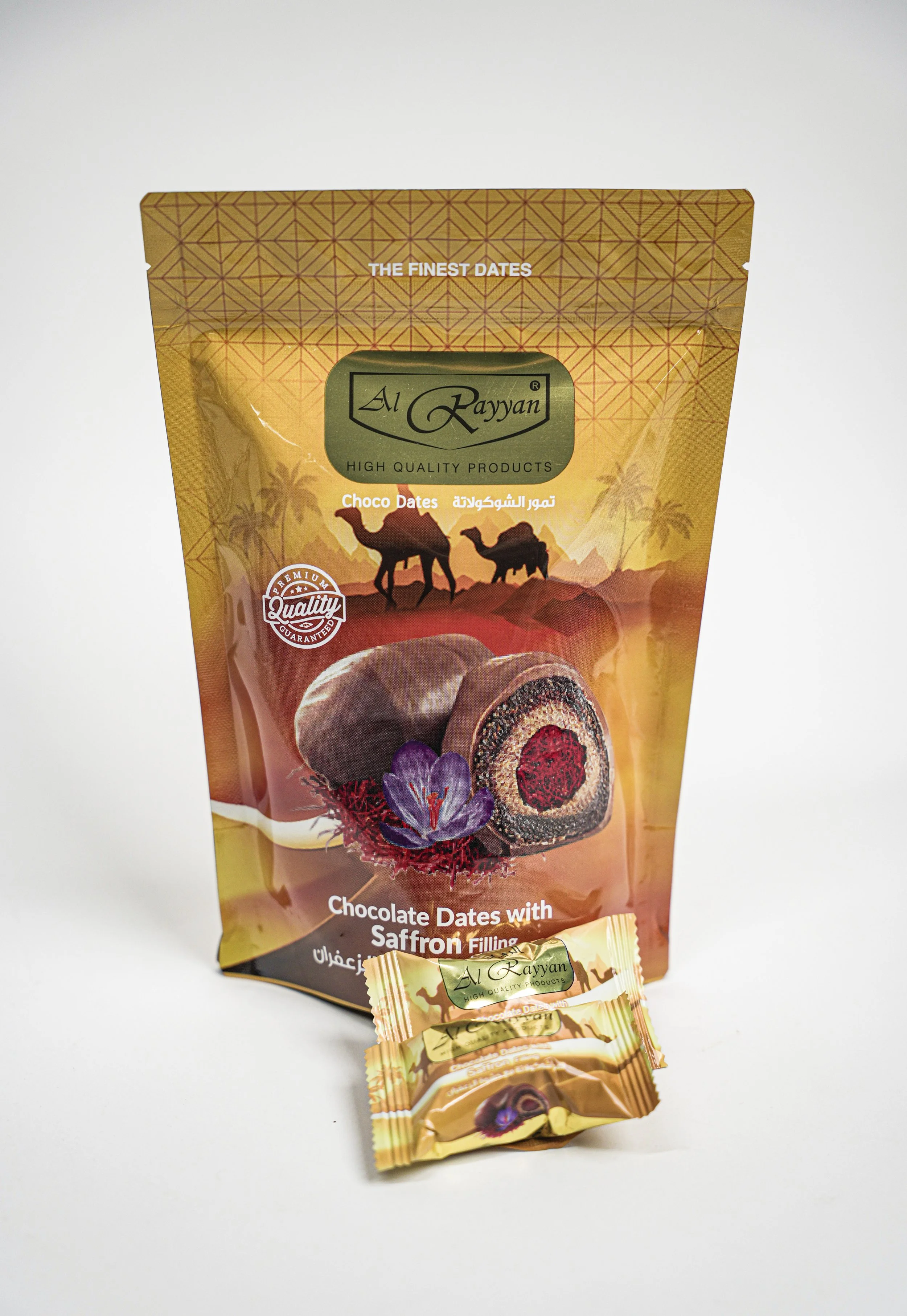 Packaging of Al Rayyan chocolate dates with saffron filling, featuring a desert scene with camels and palm trees, a large date with chocolate and saffron filling, and a single wrapped date piece.