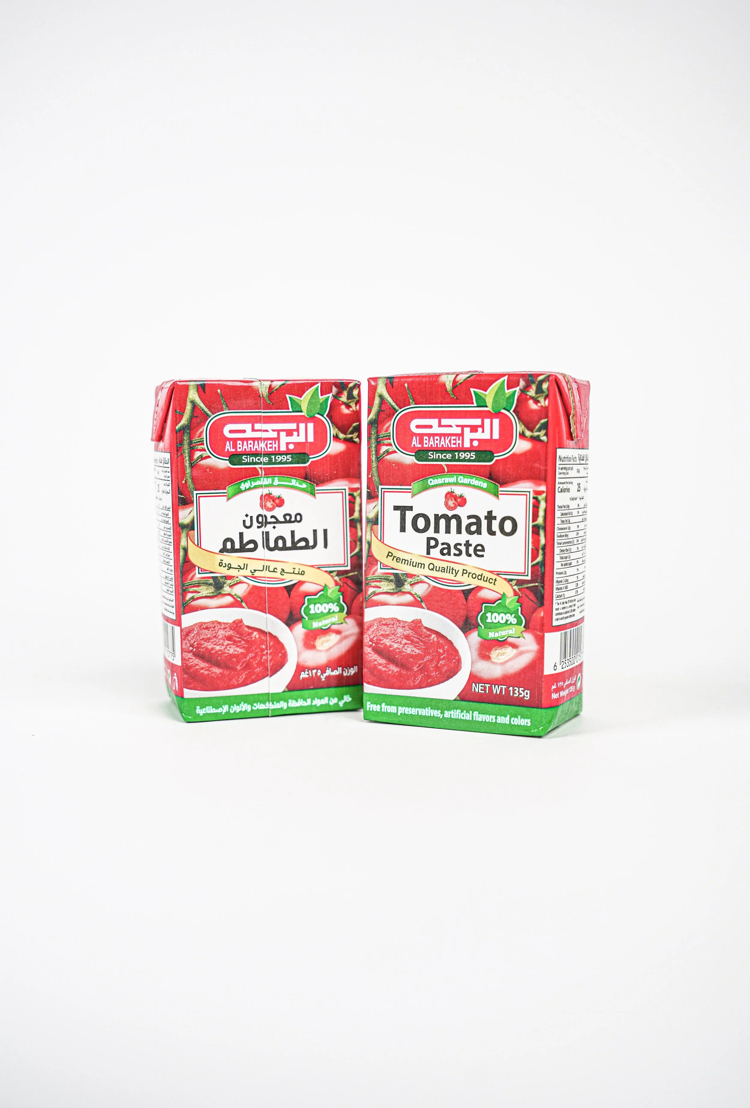 Two cartons of Al Barakeh tomato paste, one with Arabic text and the other with English, placed on a white surface against a white background.