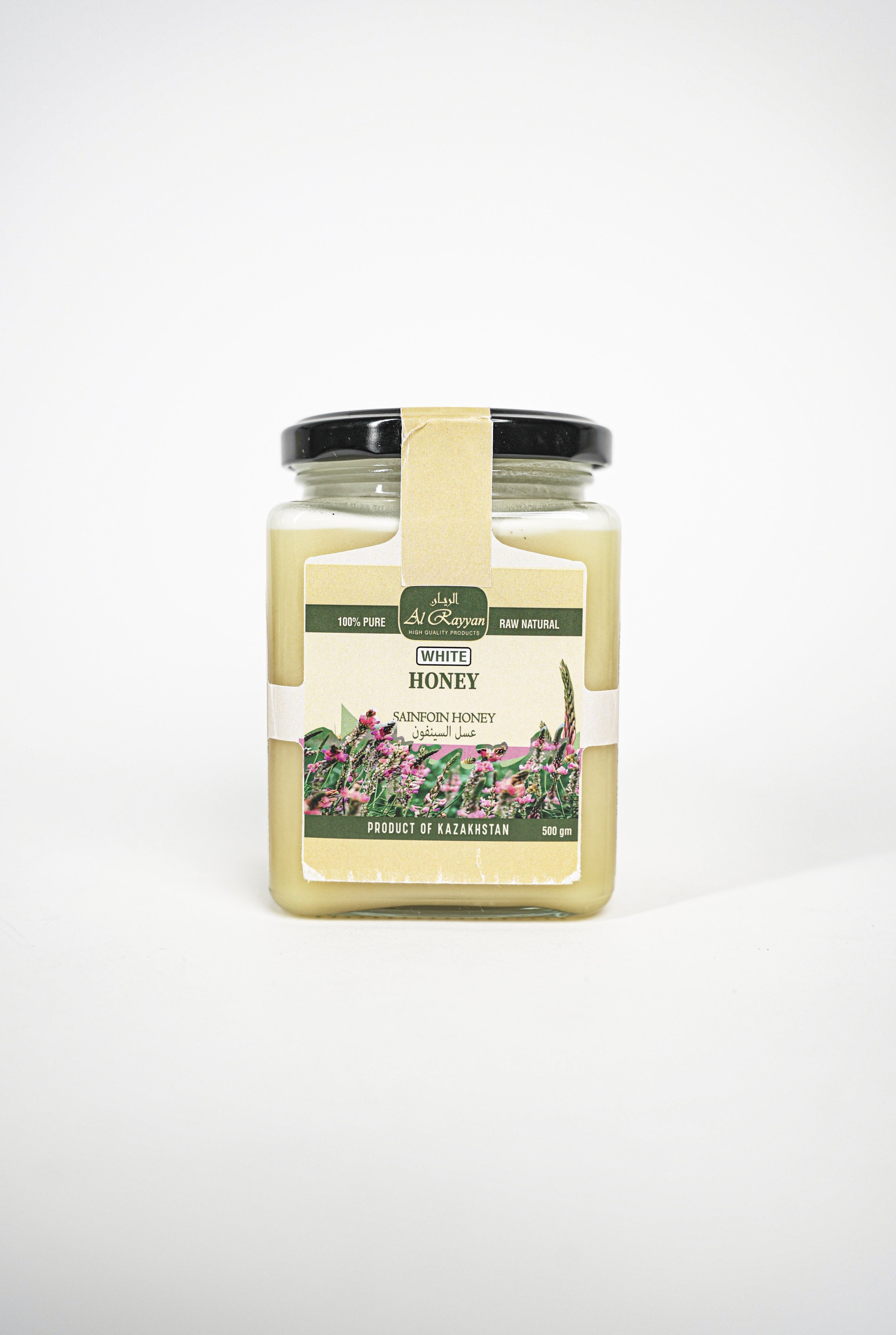 A jar of white honeysuckle honey from Kazakhstan with a black lid and a beige label featuring green accents and floral illustrations.