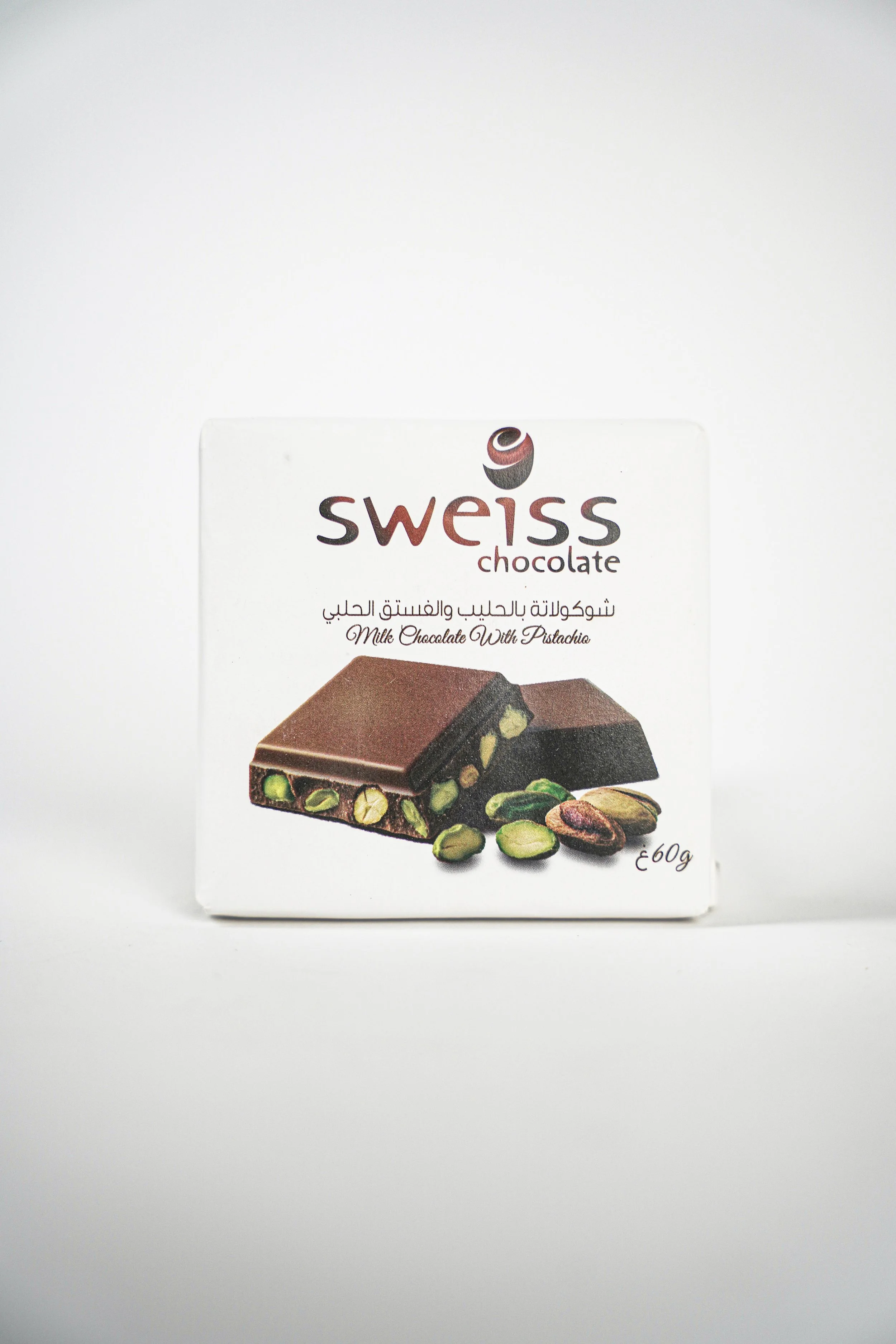 A white box of Swiss chocolate with pistachios, featuring a picture of the chocolate on the front and text in English and Arabic.