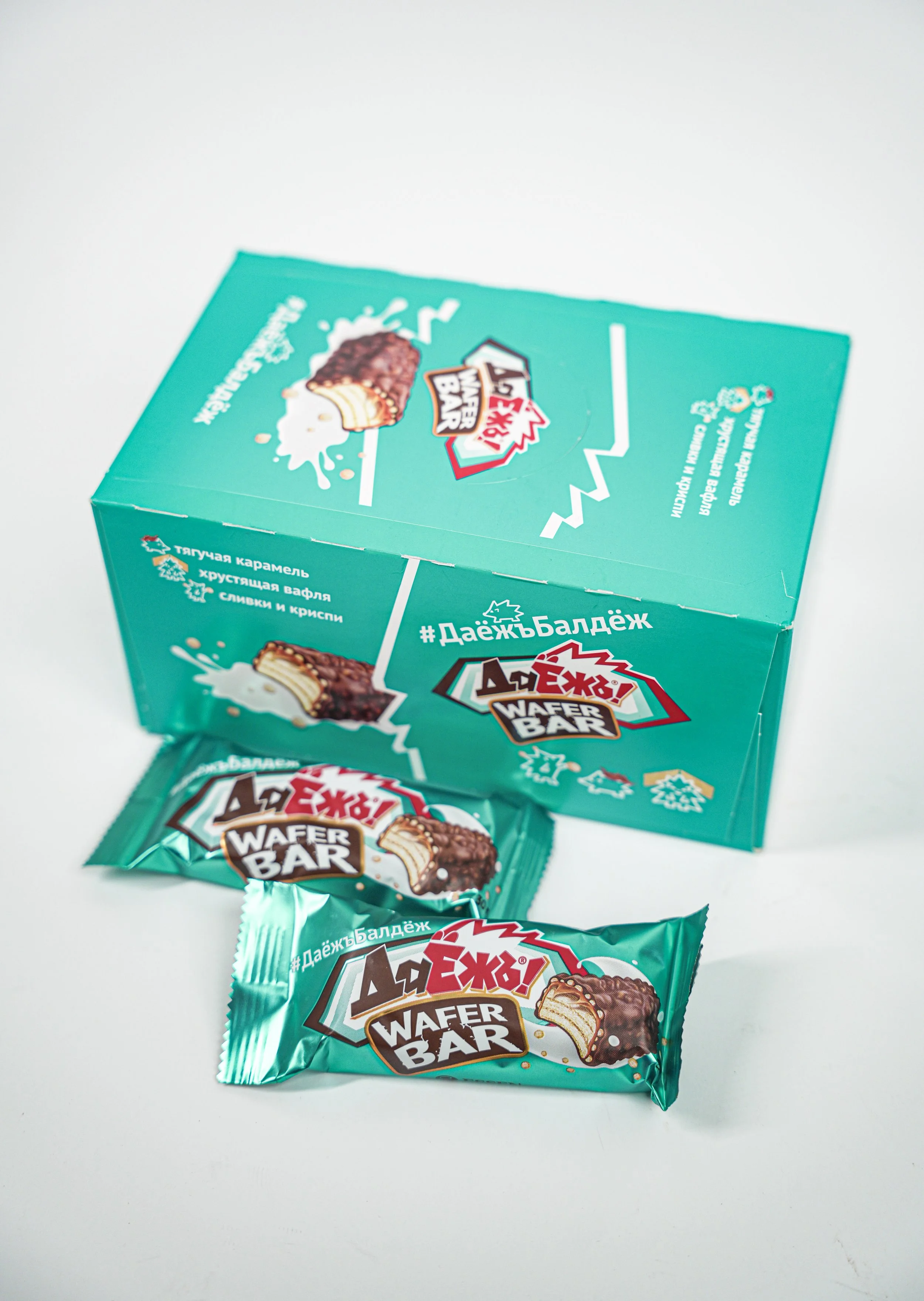 A turquoise box and two individually wrapped wafer bars labeled #Д_addьБалдёж, with illustrations of a wafer bar and snowflakes on the packaging, placed on a white surface.