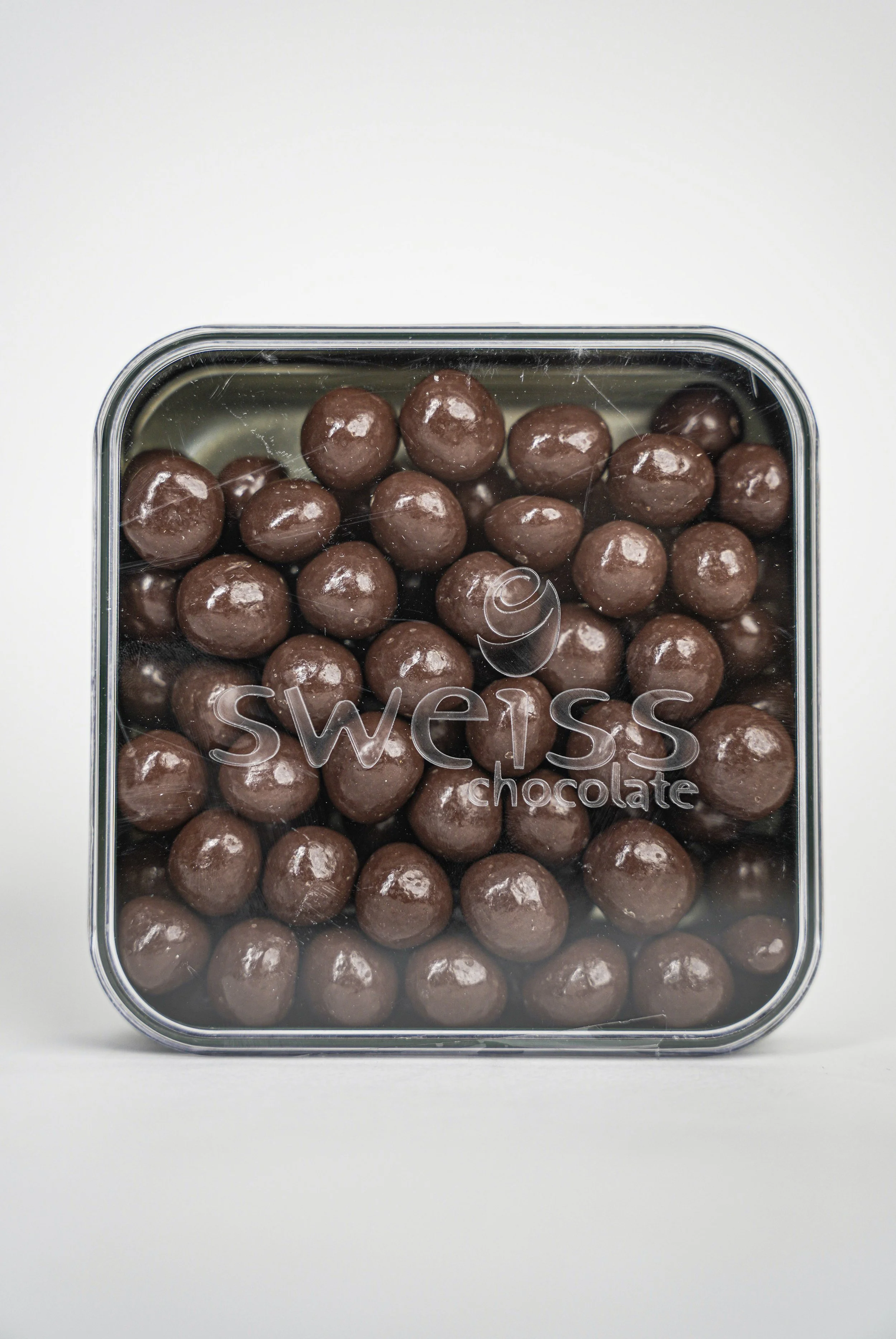 A clear plastic container of Swiss chocolate balls with a black and white label.