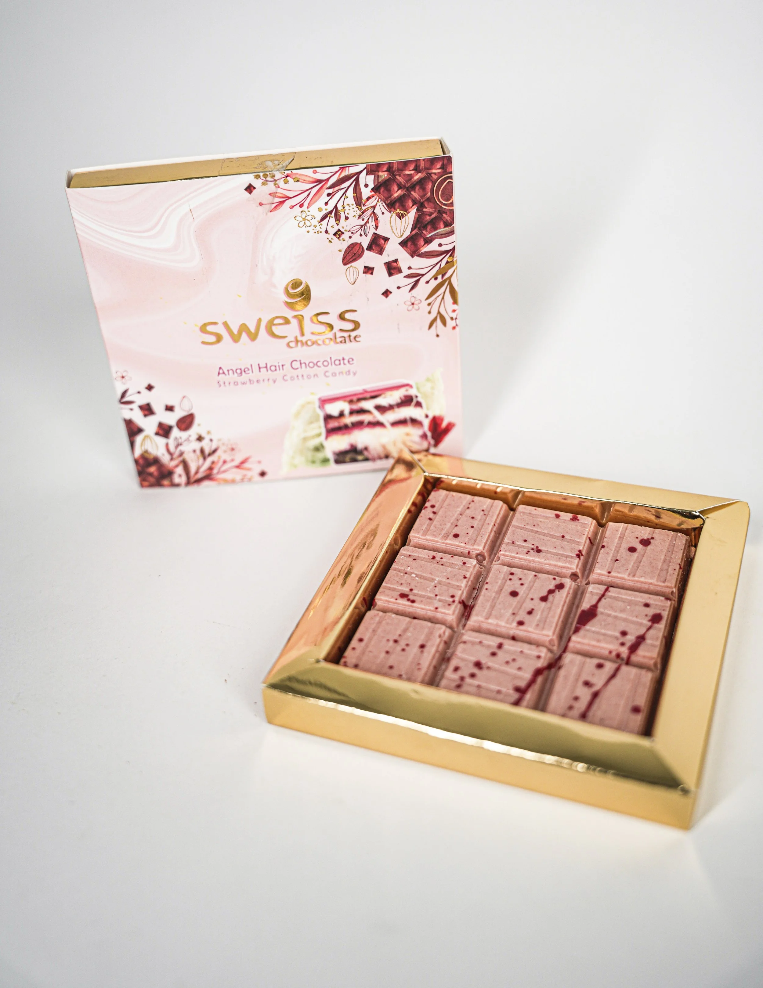 Swiss Angel Hair Chocolate with a decorative pink and gold packaging, featuring a picture of layered strawberry cotton candy-flavored cake