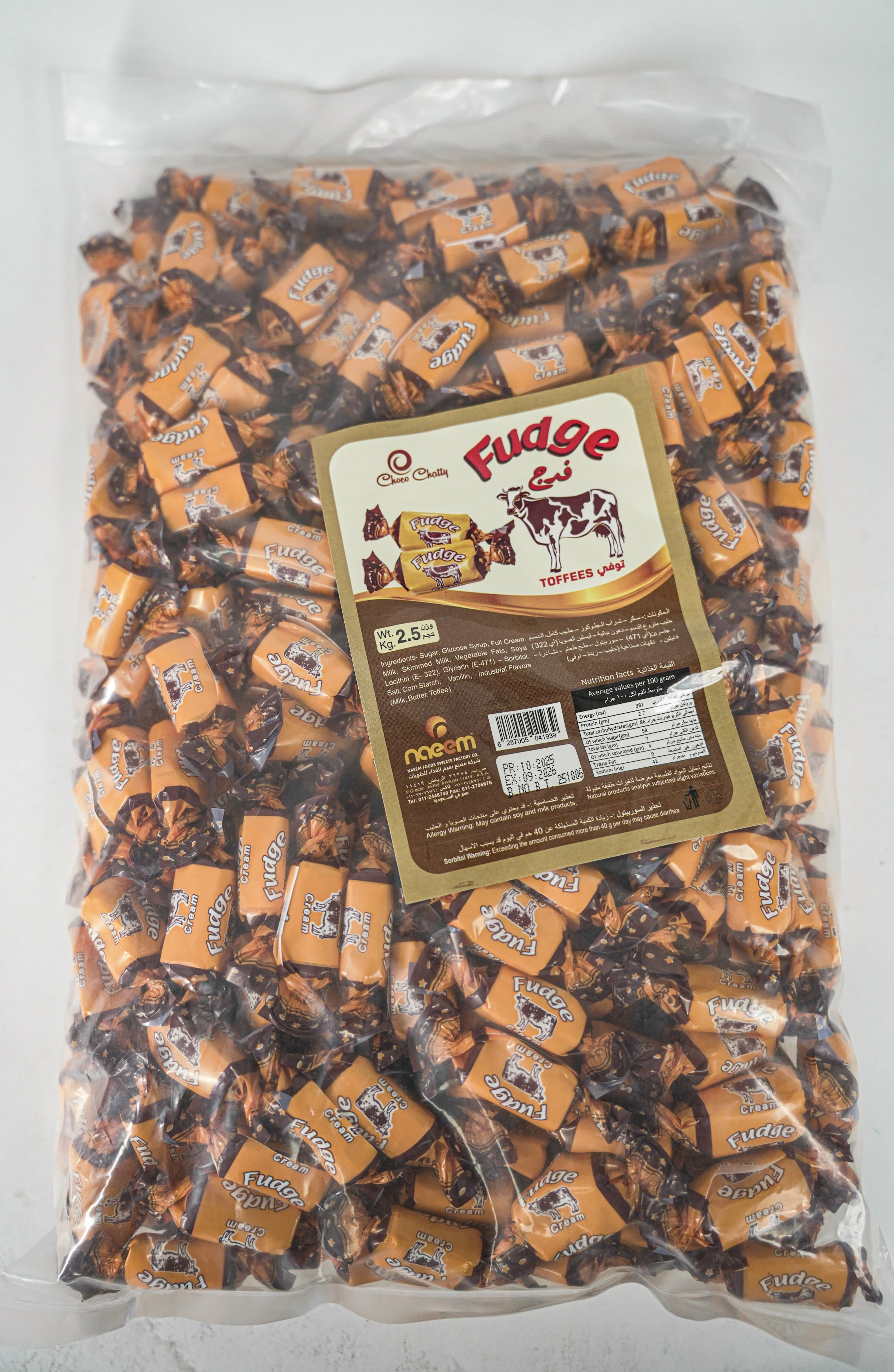 A large transparent plastic bag filled with individually wrapped orange and black cows and fudge candies with a label in Arabic and English.