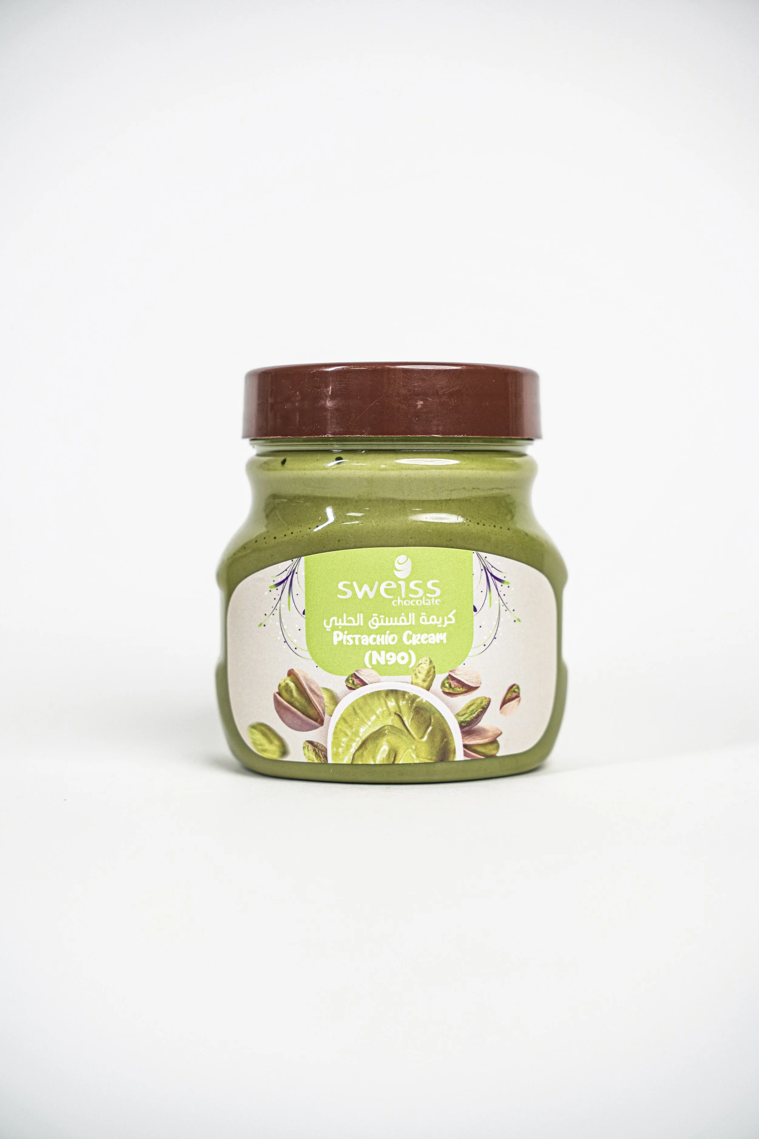 A jar of Swiss chocolate pistachio cream with a brown lid and green label showing pistachio nuts and cream.