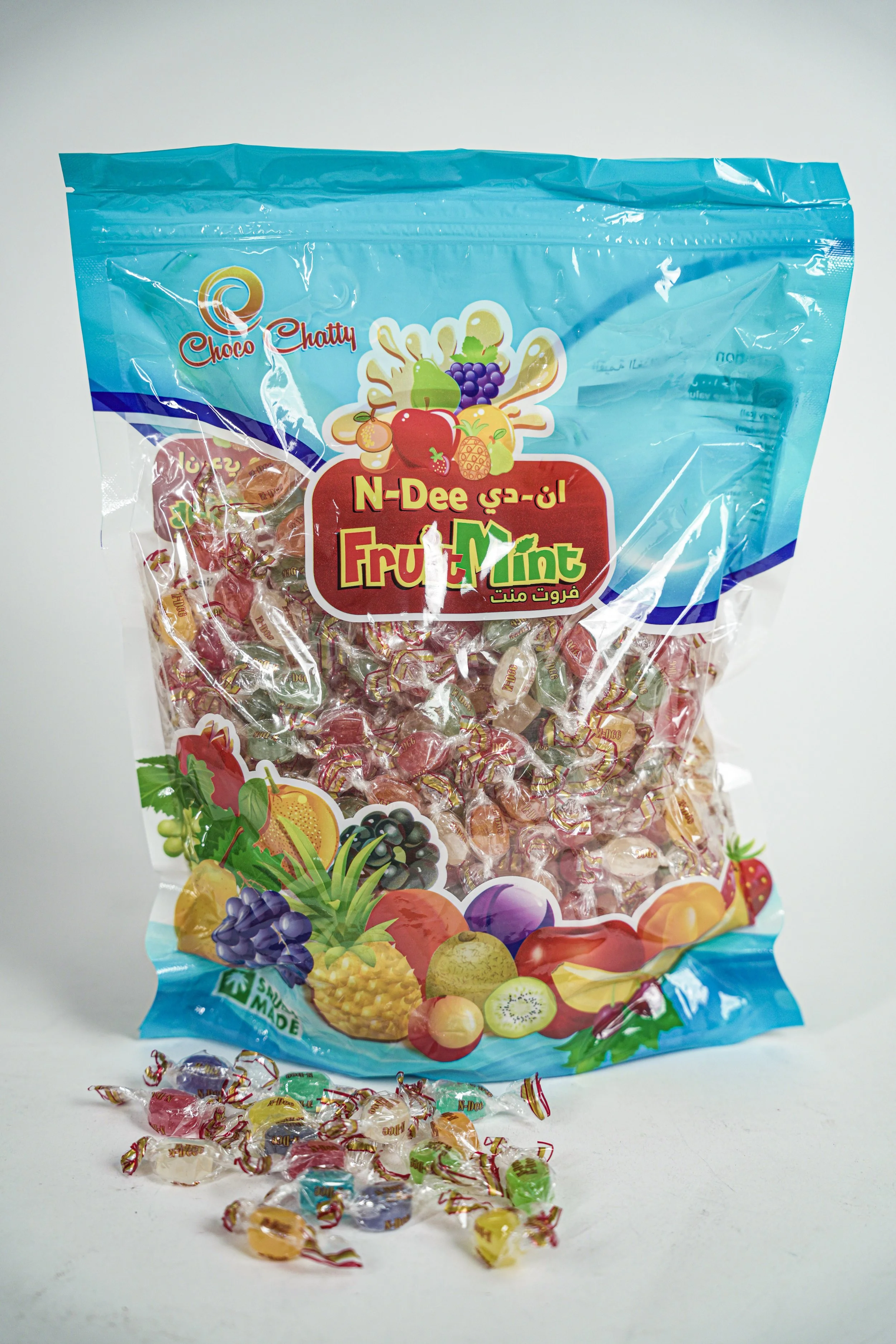 A large transparent bag of assorted fruit-flavored candies with colorful fruit illustrations on the packaging and individual candies in various colors scattered in front.