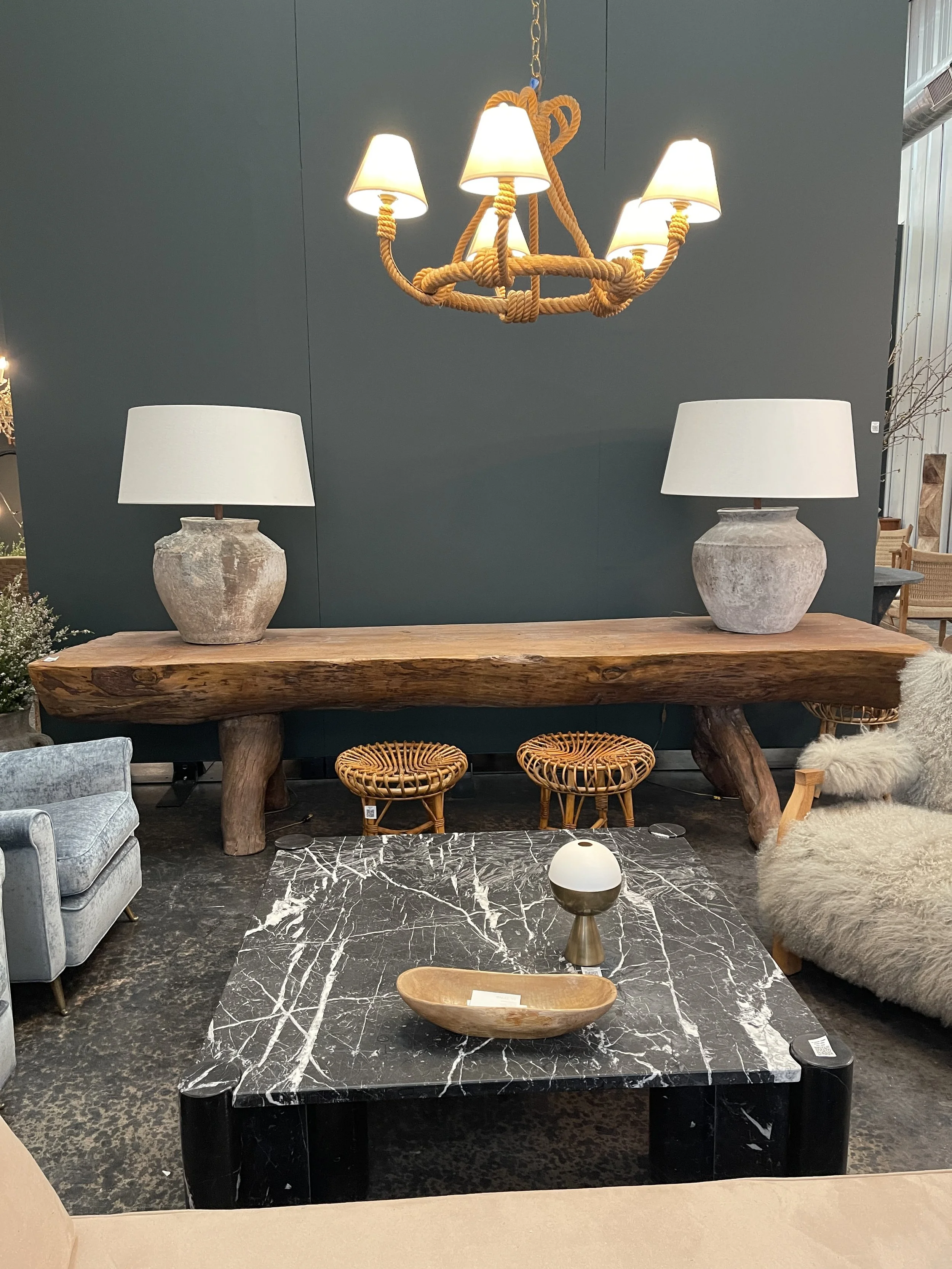 Living room with black marble coffee table, gray armchair, white table lamps, wooden console table, and a black wall with a gold chandelier with six lamps hanging from a chain.