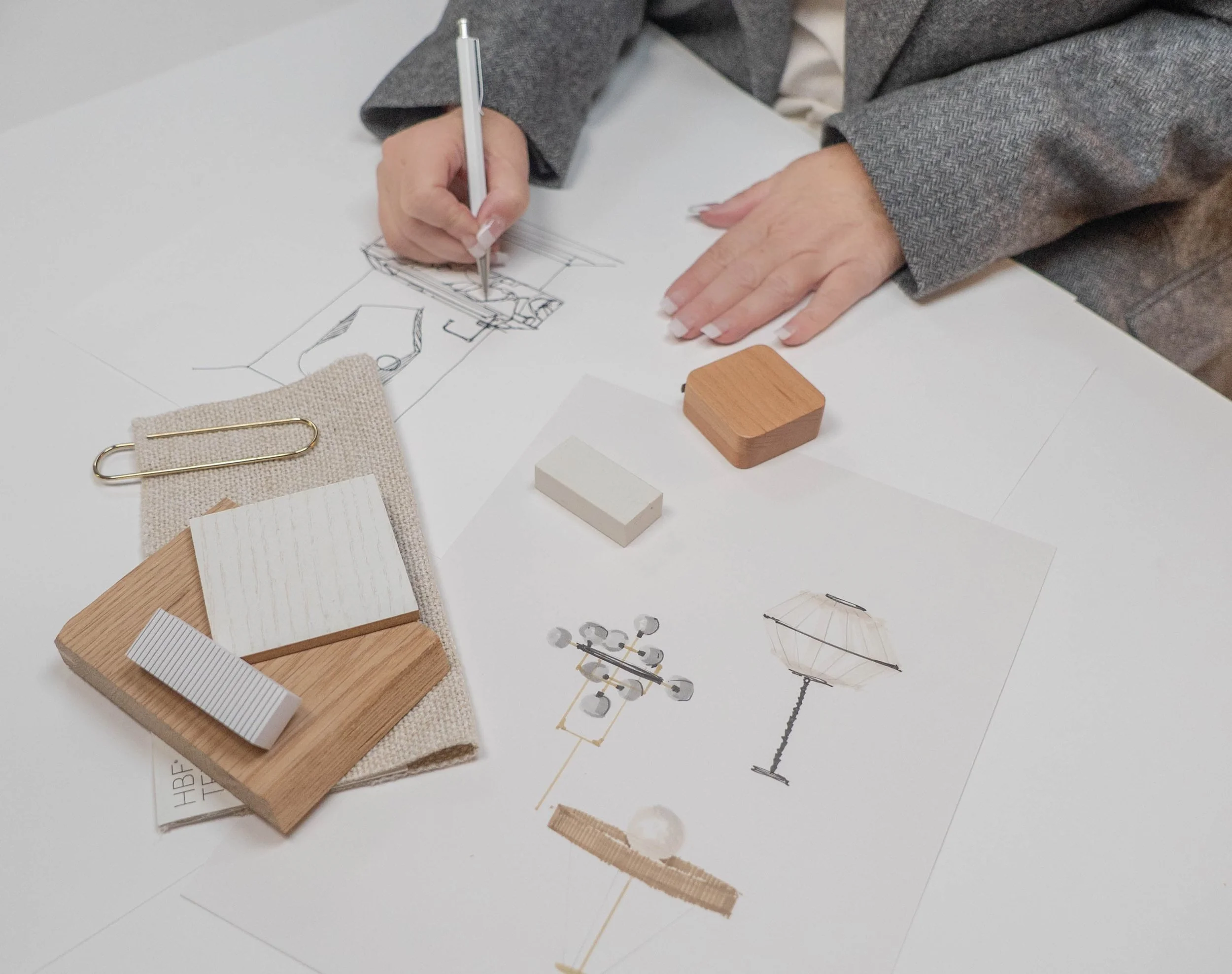 Person designing a space with sketches, fabric samples, and model materials on a white table.