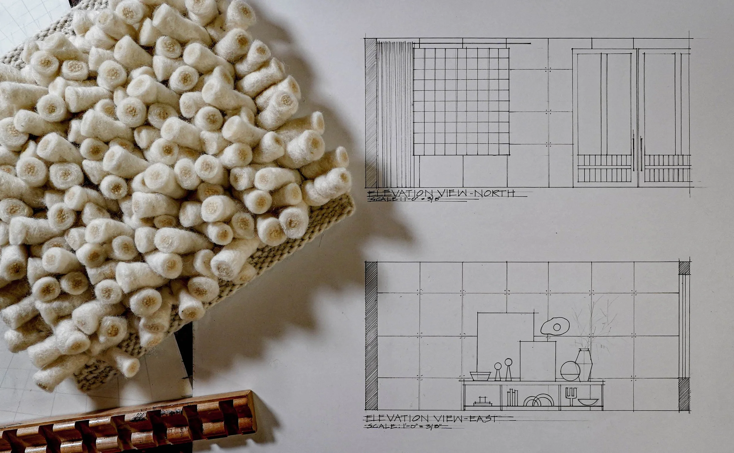 A large bundle of cotton swabs placed on top of architectural blueprints, with a wooden comb and a woven fabric in the background.