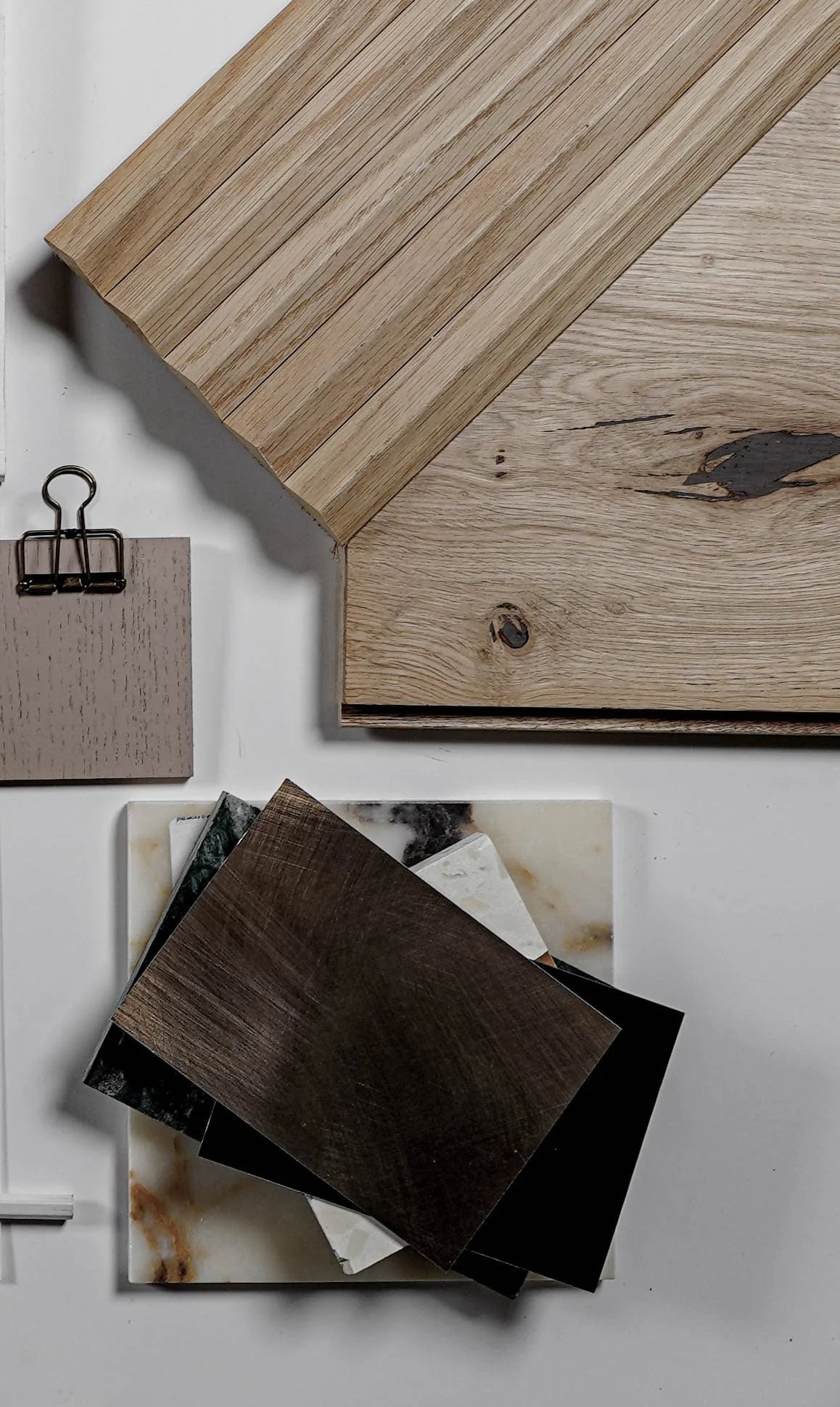 Arrangement of wooden and marble samples, including a light wood plank, darker wood tiles, and marble slabs on a white surface.