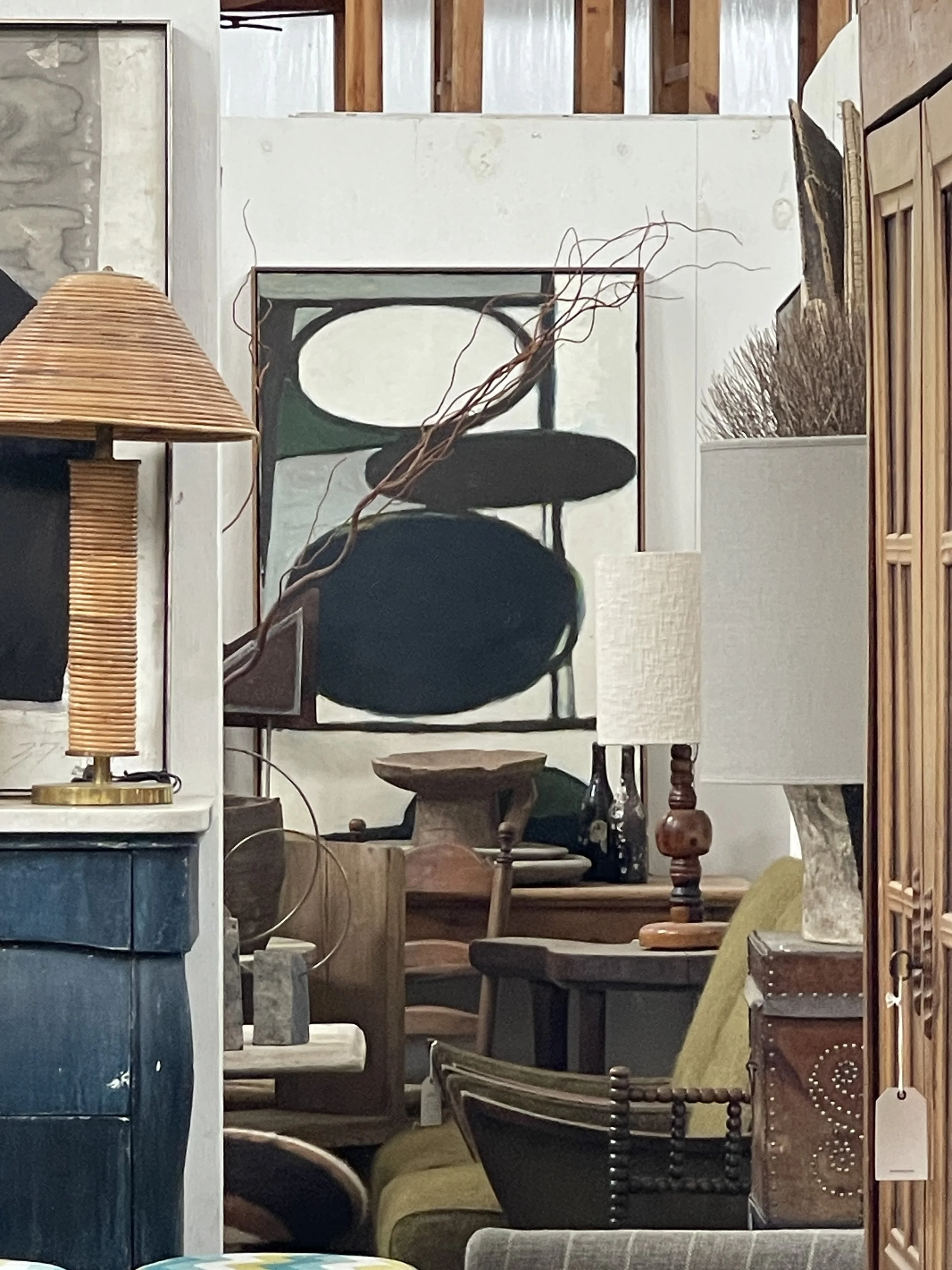 Collection of various furniture and decorative items inside a store, including lamps, chairs, and a framed artwork in the background.