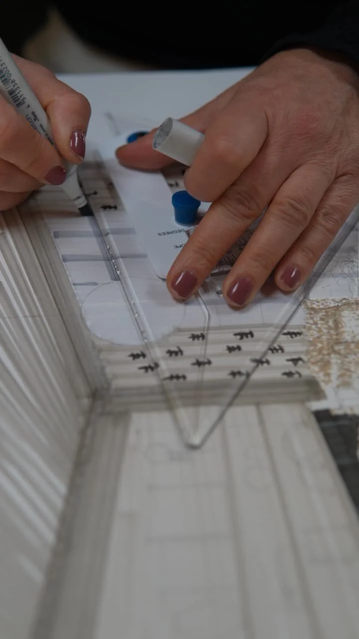 Close-up of hands using a clear triangular ruler and a marker to measure and mark a piece of architectural woodwork or molding.