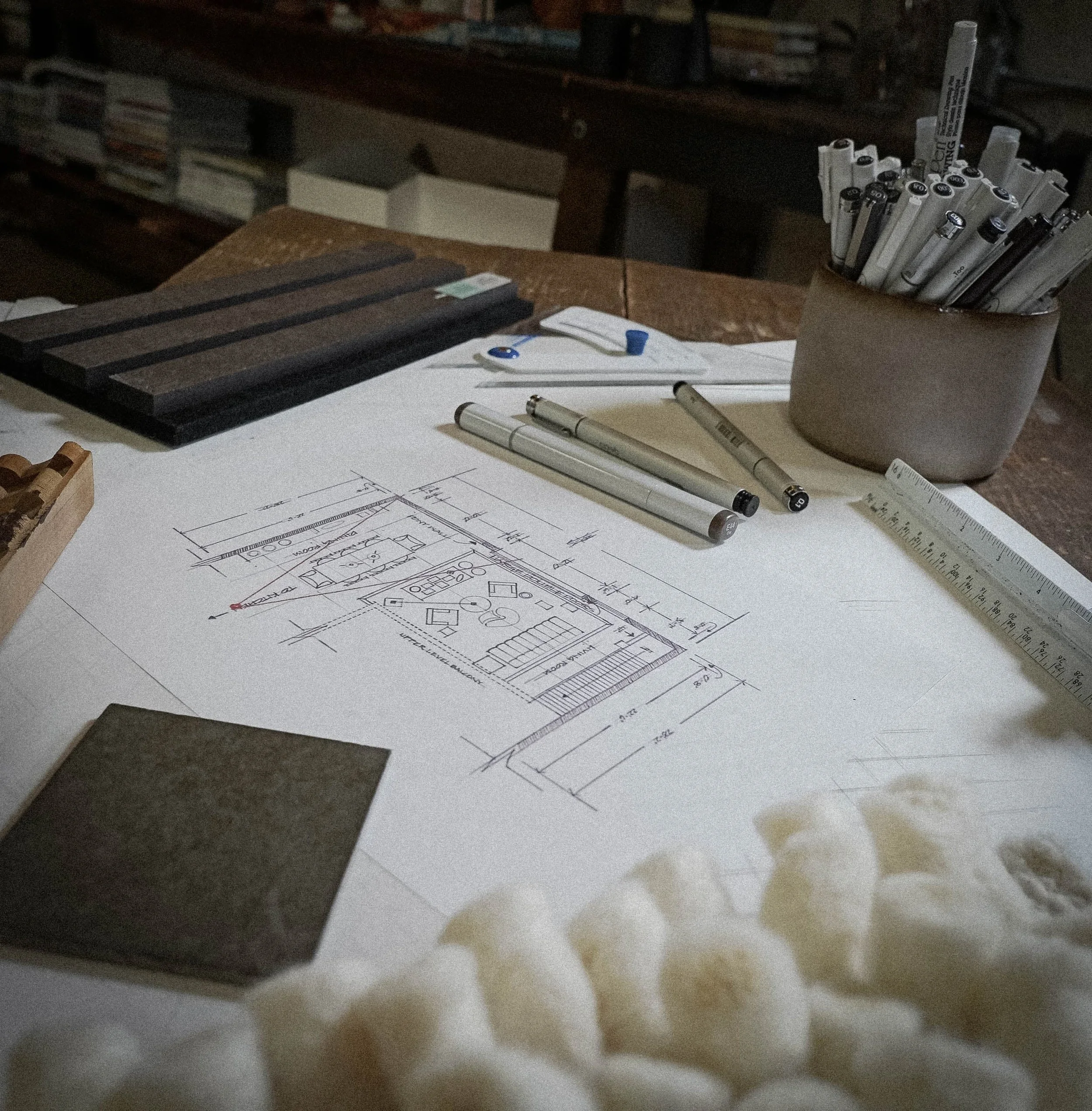 Architectural blueprint or floor plan on a desk with drawing tools including pens, rulers, and notebooks.