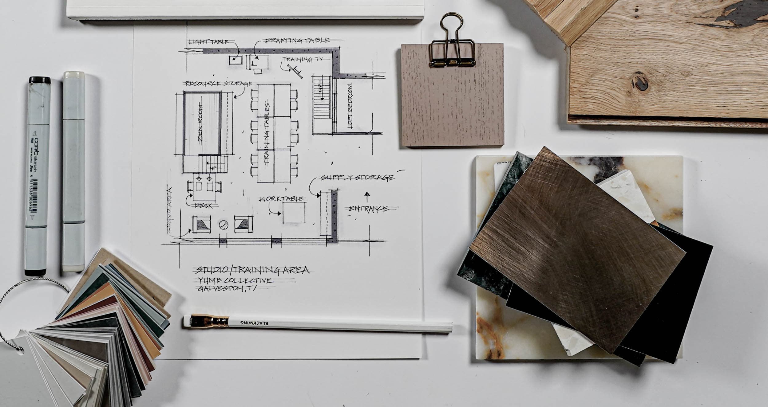 Interior design workspace with a floor plan sketch, color and material samples, color markers, a pencil, and sample boards for interior materials.
