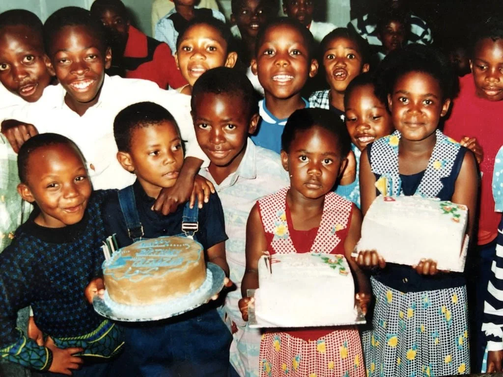 Group of joyful children celebrating around birthday cakes in a brightly lit room, symbolizing innocence, community and the joy of shared rituals; part of High Risqué’s human moments archive.