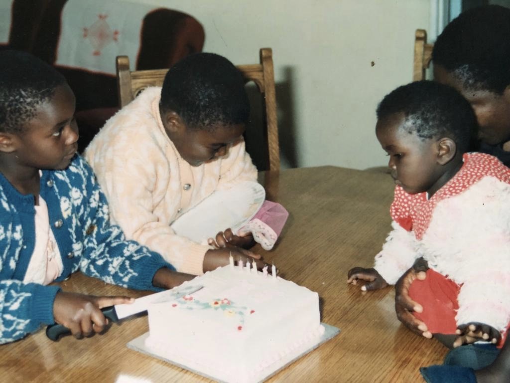 Children gathered around a birthday cake with lit candles, celebrating a birthday party.