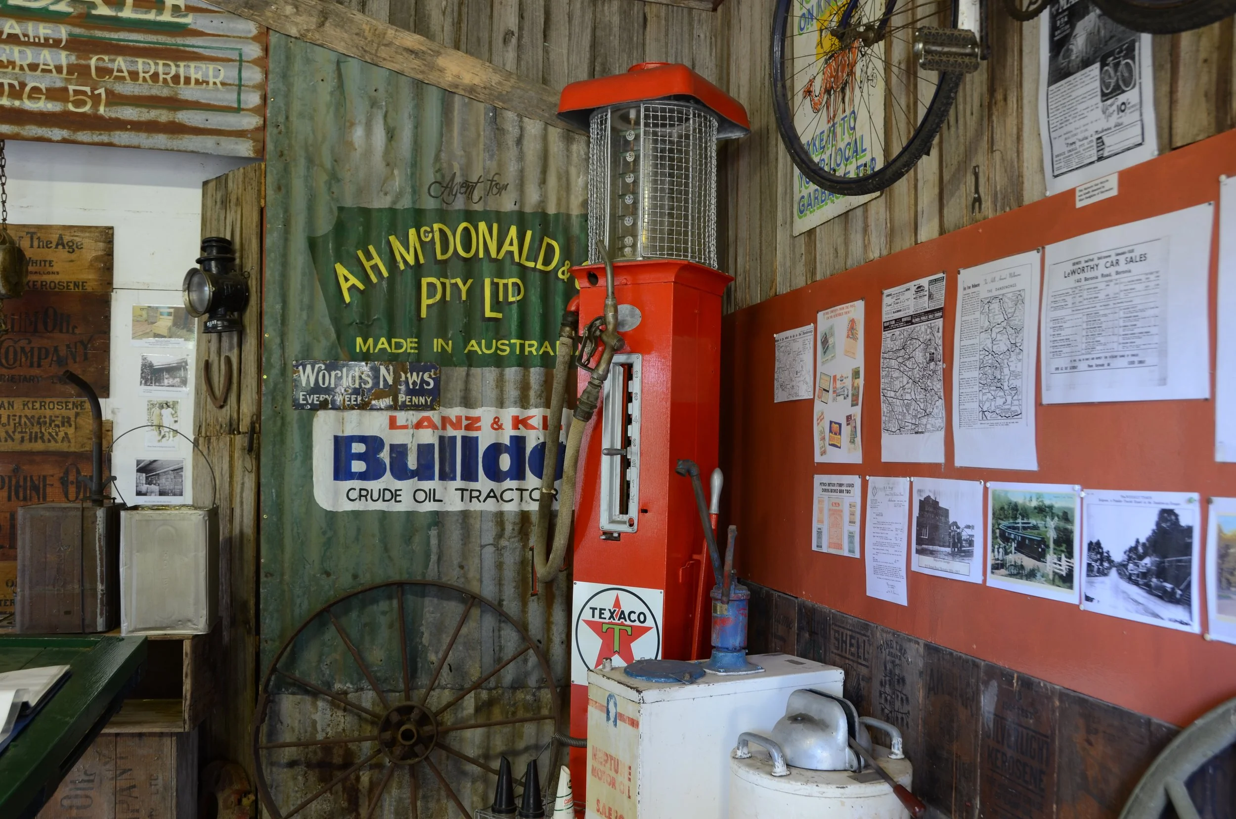 Vintage gas pump with red casing and metal grid, Texaco logo, surrounded by nostalgic signs and vintage items in an old-fashioned store or garage.