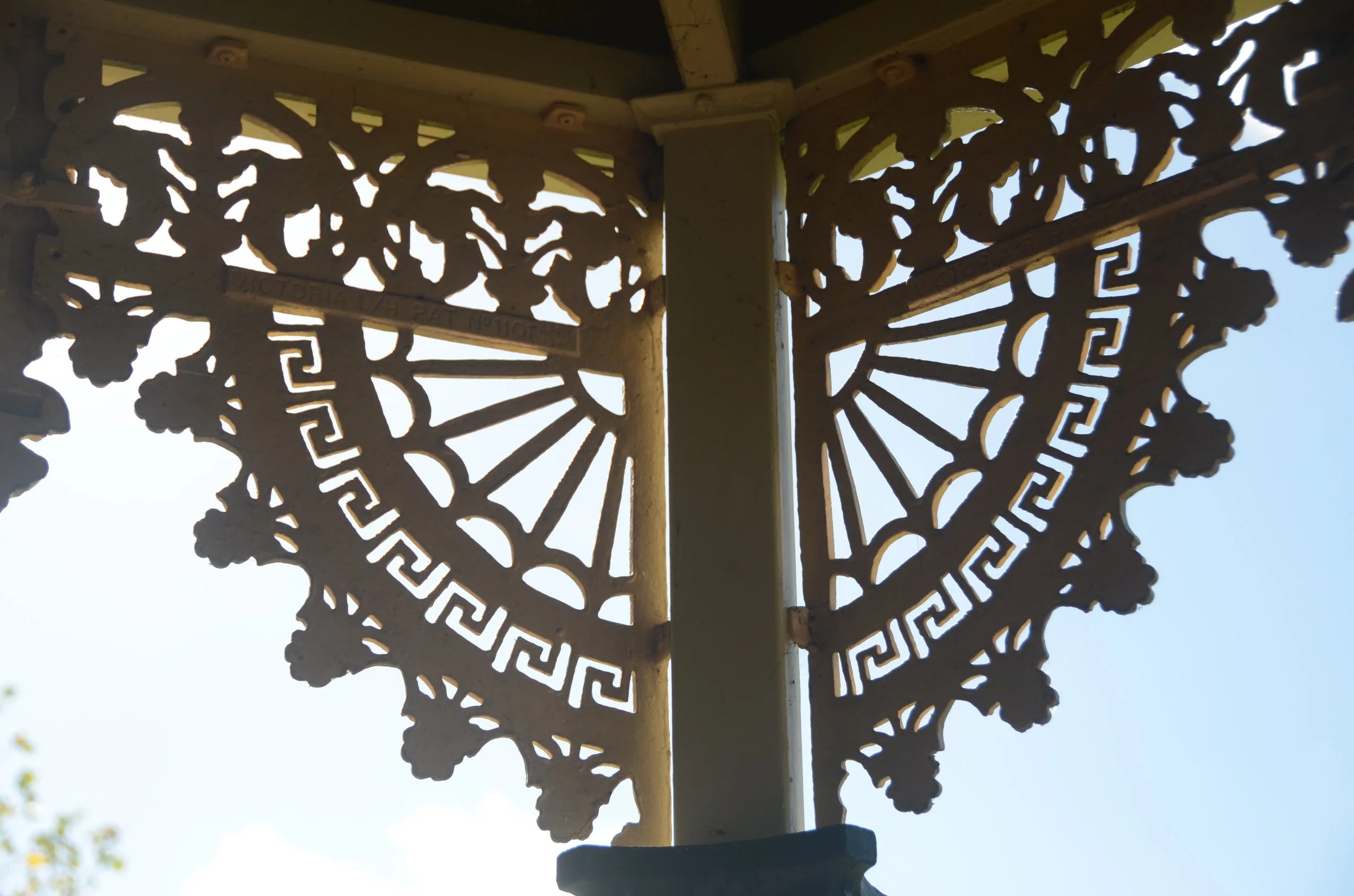 Close-up of ornate lattice woodwork at the top of a historic structure, with the sky visible through the intricate cut-out patterns.